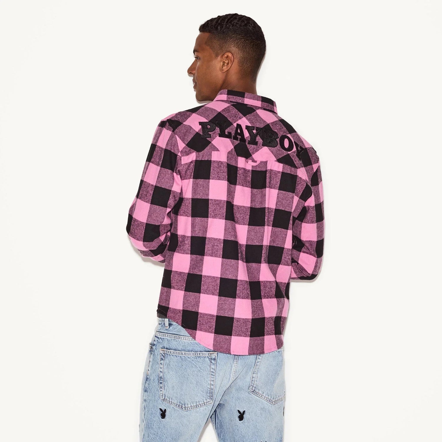 Man wearing pink and black plaid flannel long sleeve shirt with logo on back, light wash jeans