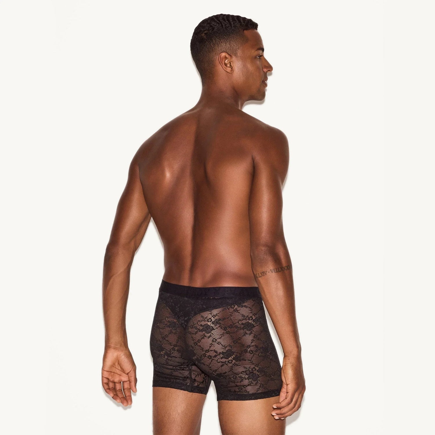 Man wearing black lace boxer briefs, shown from the back against a white background.
