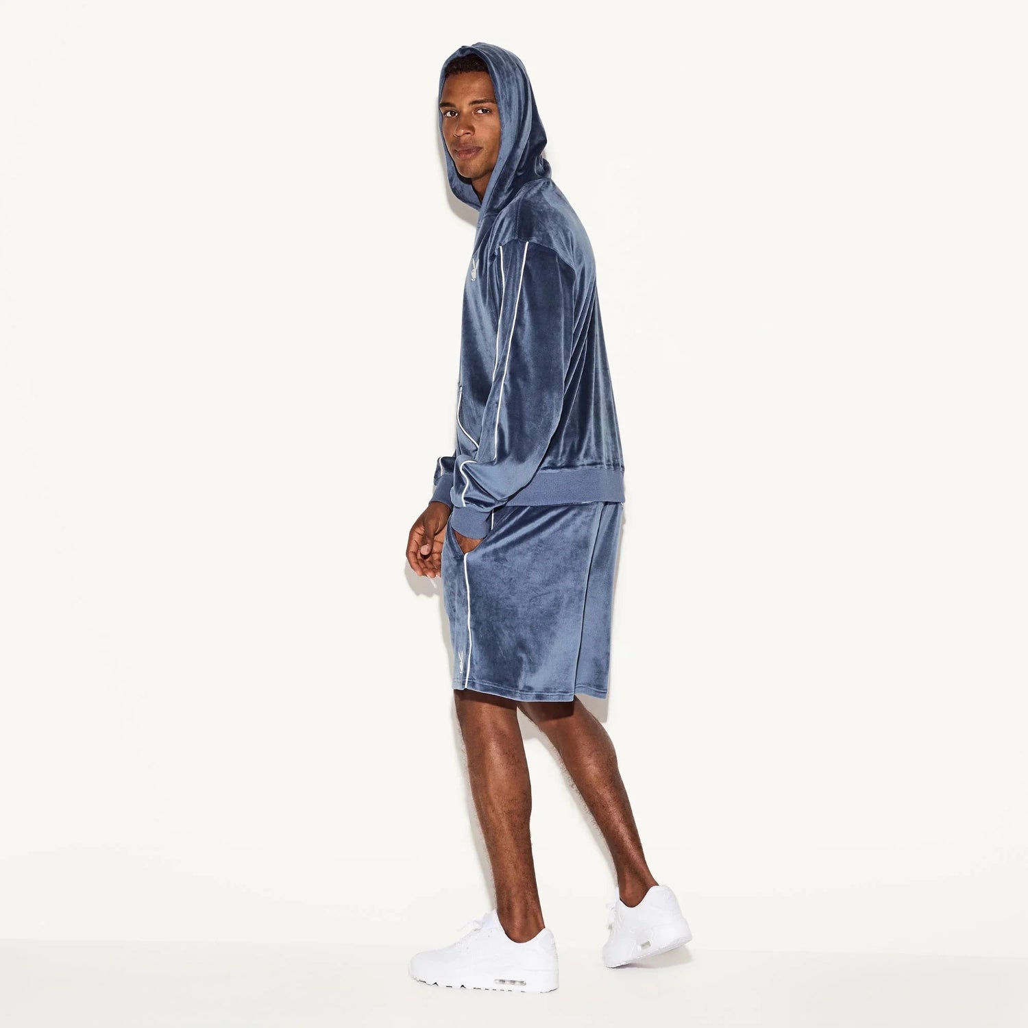 Man wearing blue velour hoodie and matching shorts set, white sneakers, on white background.