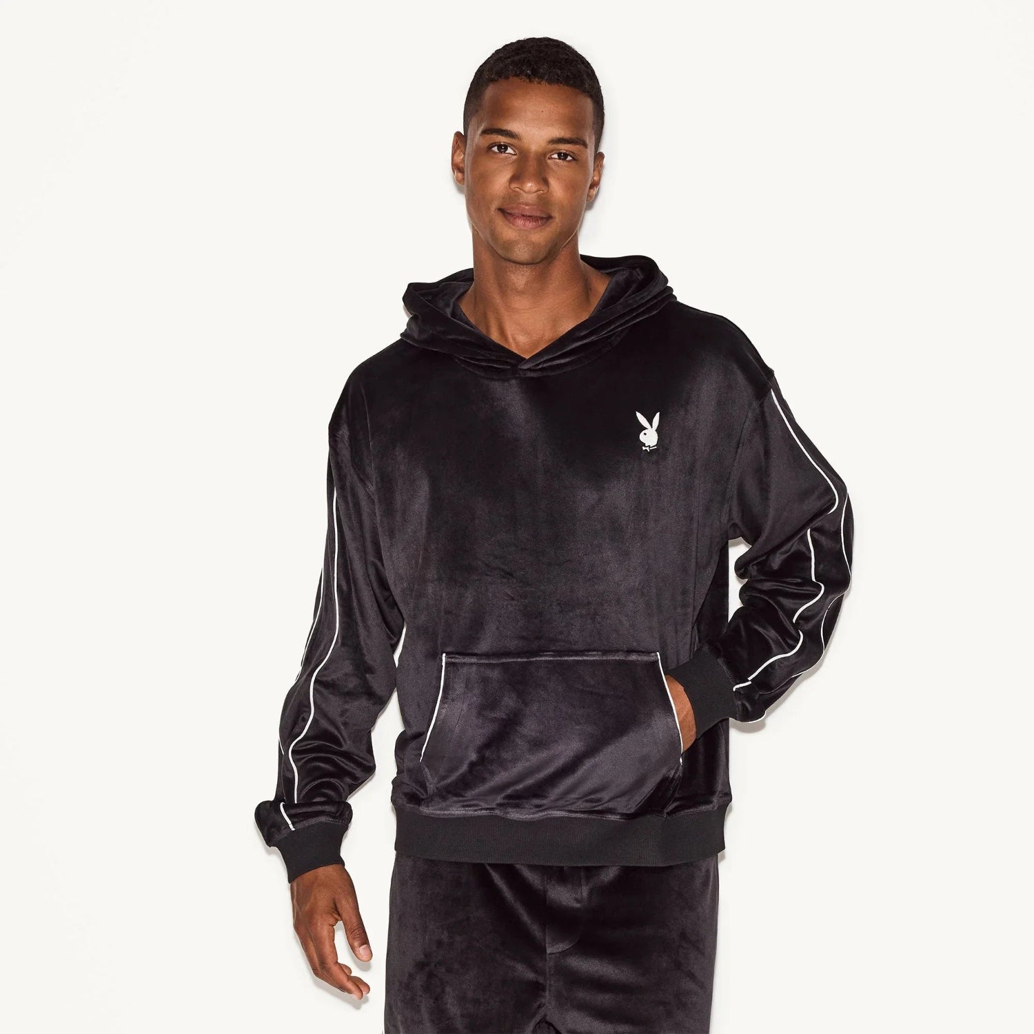 Man wearing a black velour hoodie with kangaroo pocket and white logo on chest