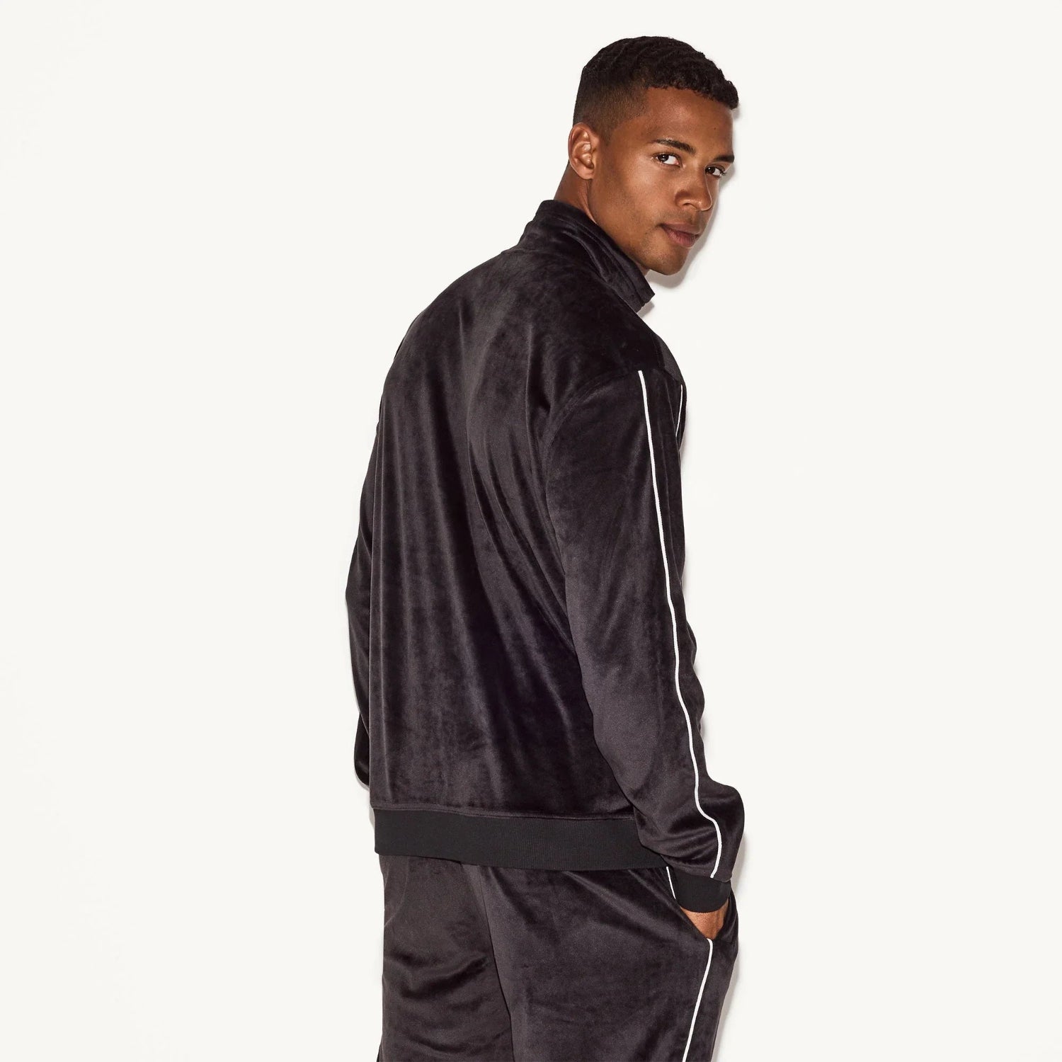 Man wearing black velour track jacket with white piping details, viewed from the back.