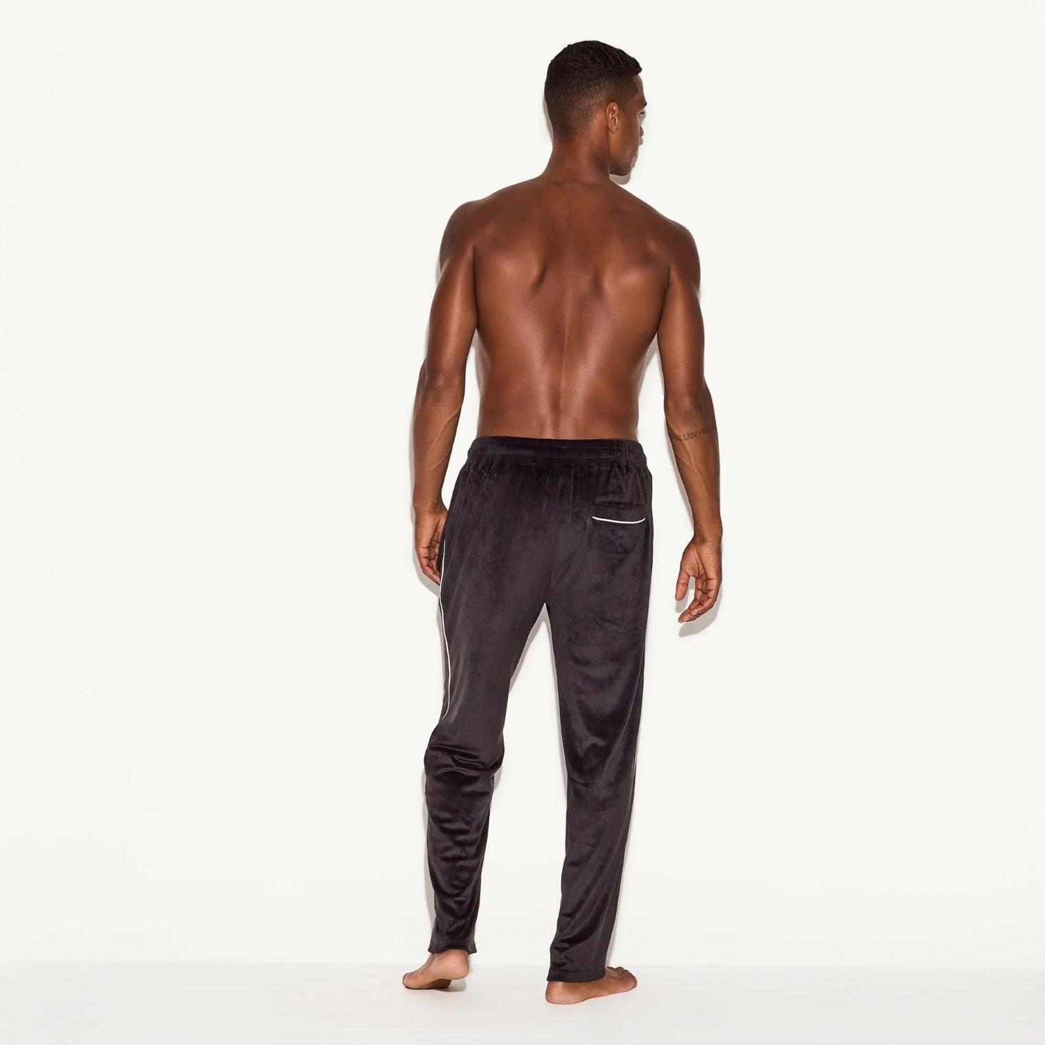 Back view of a shirtless man wearing black velour pants with a zip pocket.
