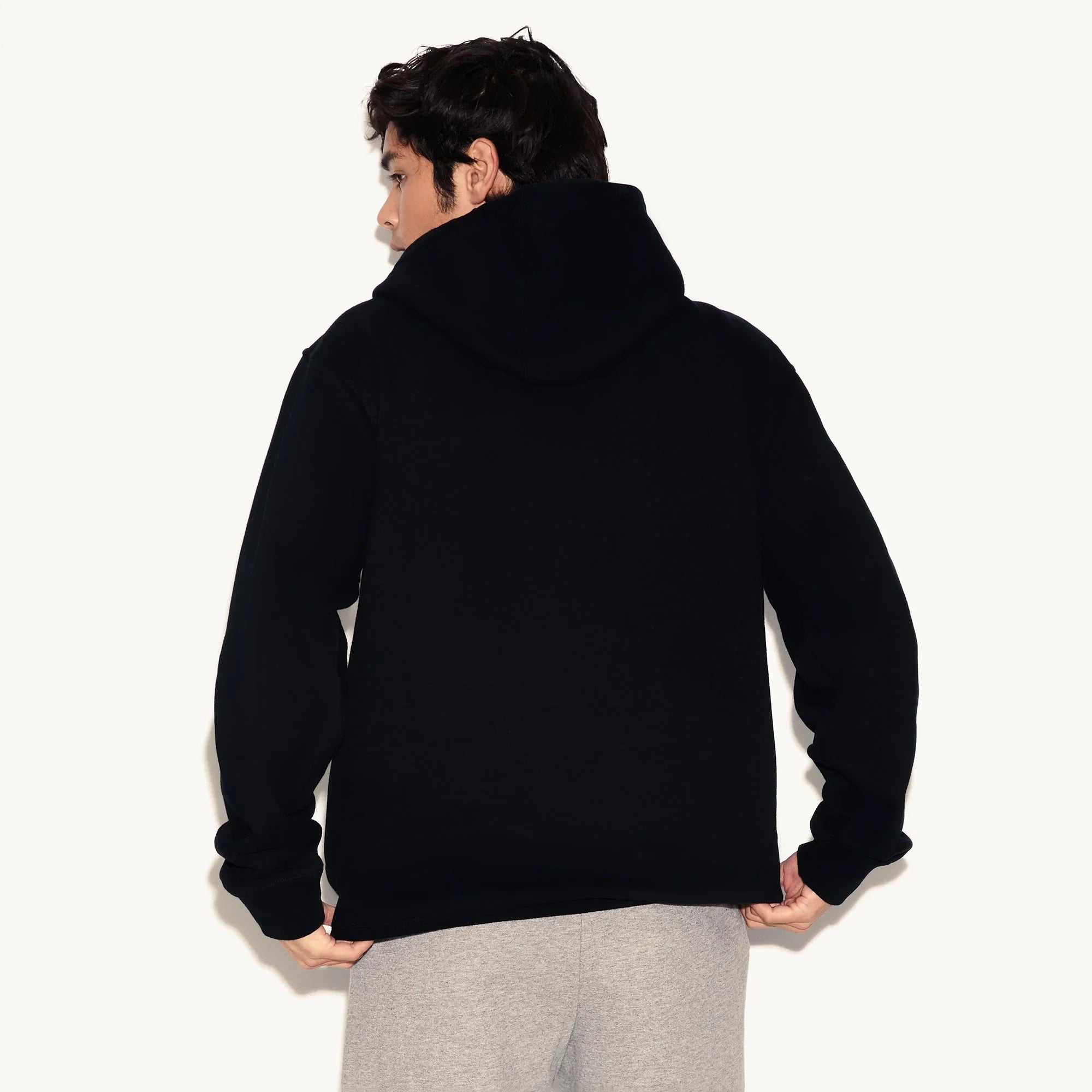 Man wearing a plain black hoodie and grey sweatpants, shown from the back