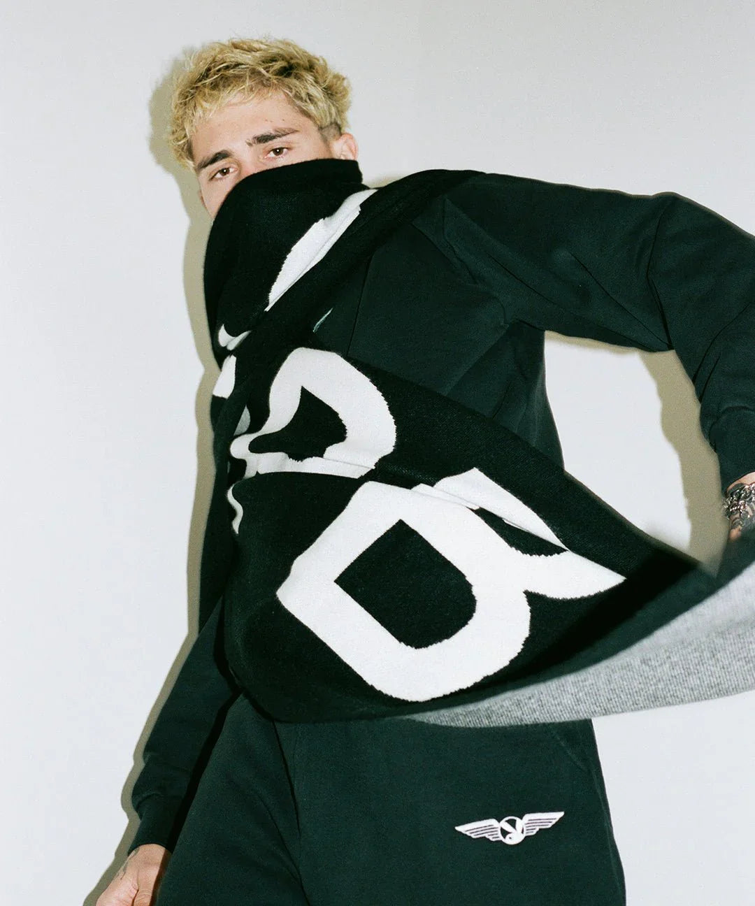 Man wearing a black and white cashmere scarf with bold lettering and matching black outfit