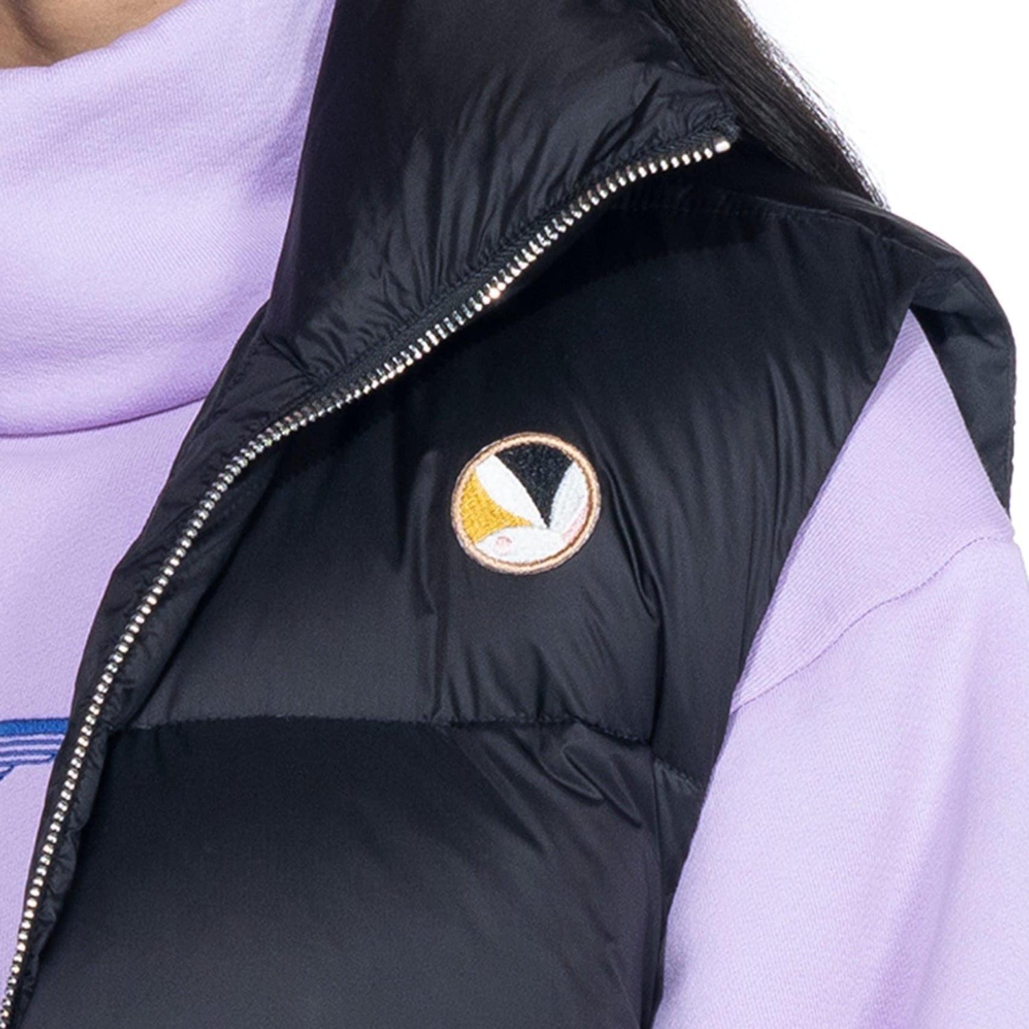 Black puffer vest with embroidered patch over lavender sweatshirt, close up view