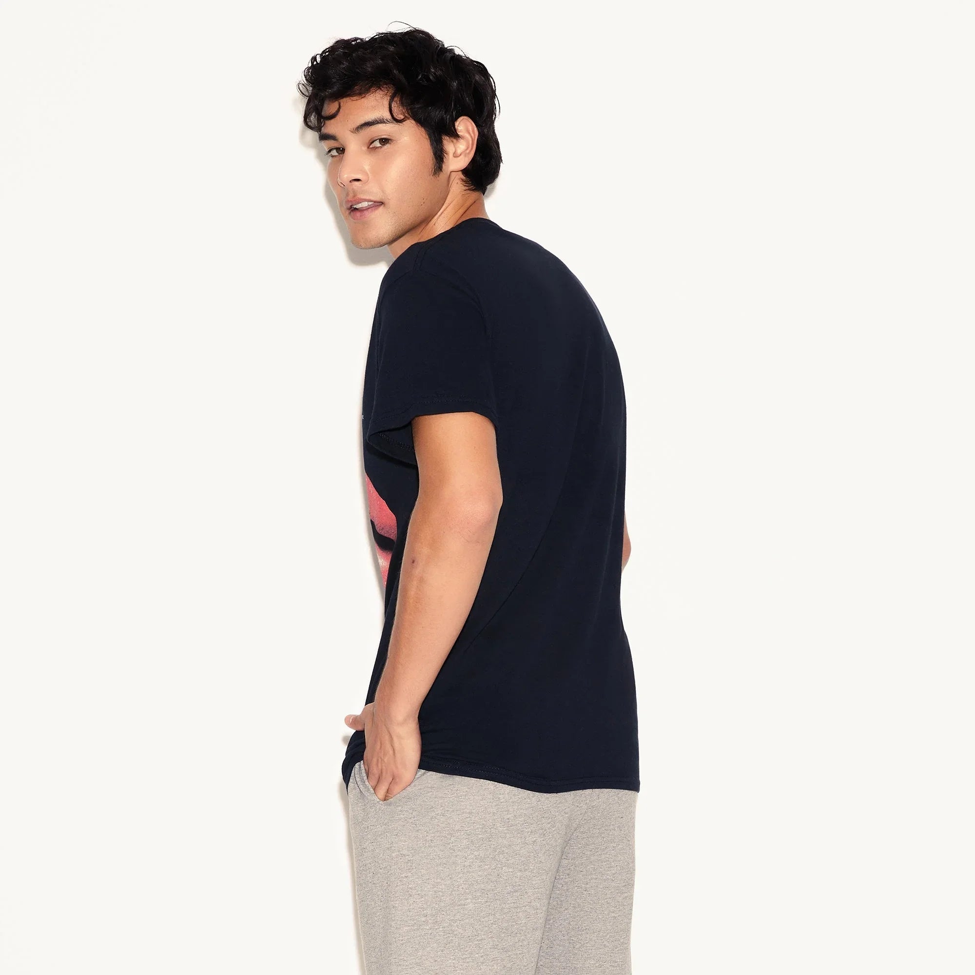 Man wearing a black graphic t-shirt and grey sweatpants standing against a white background