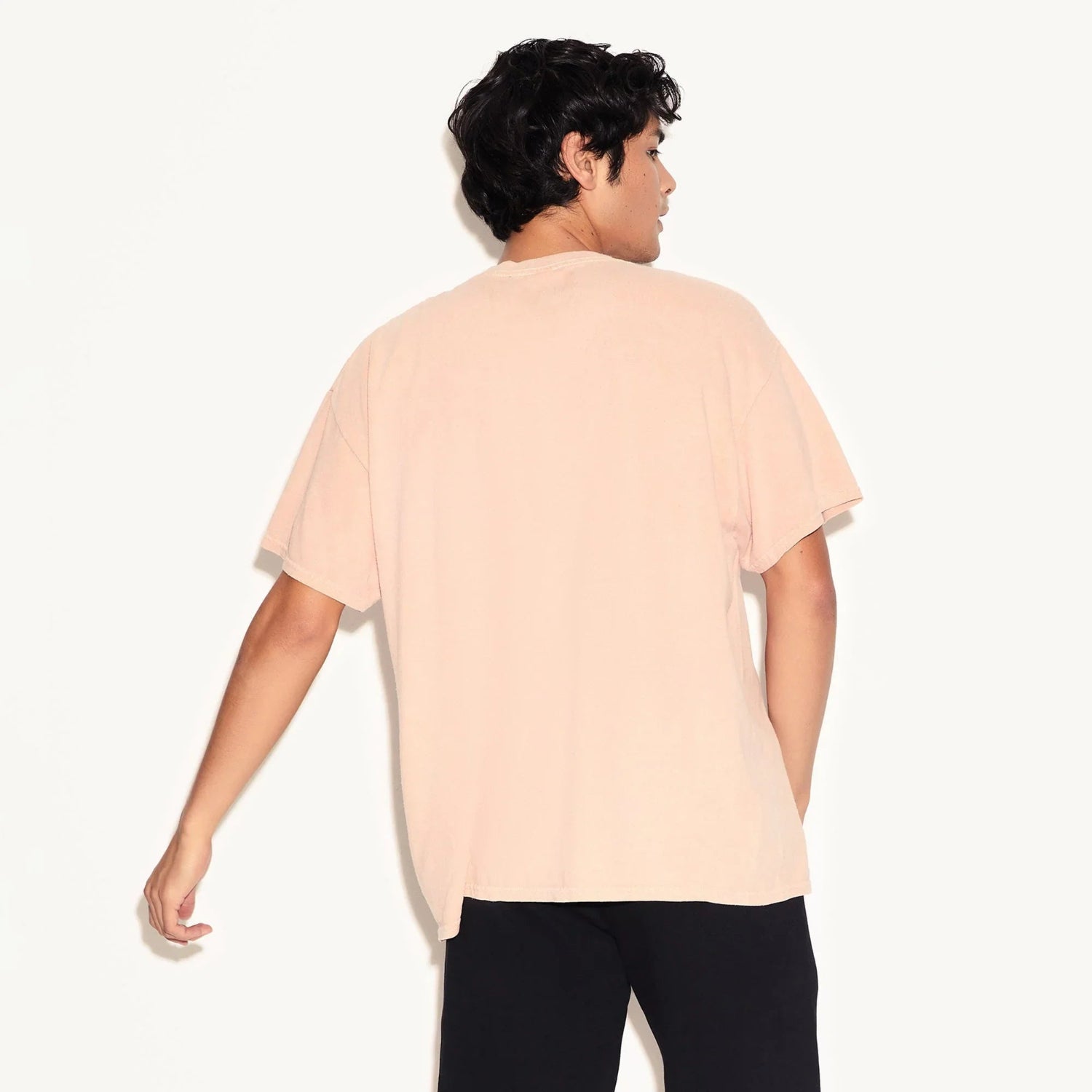 Back view of a person wearing a light pink short sleeve t-shirt and black pants