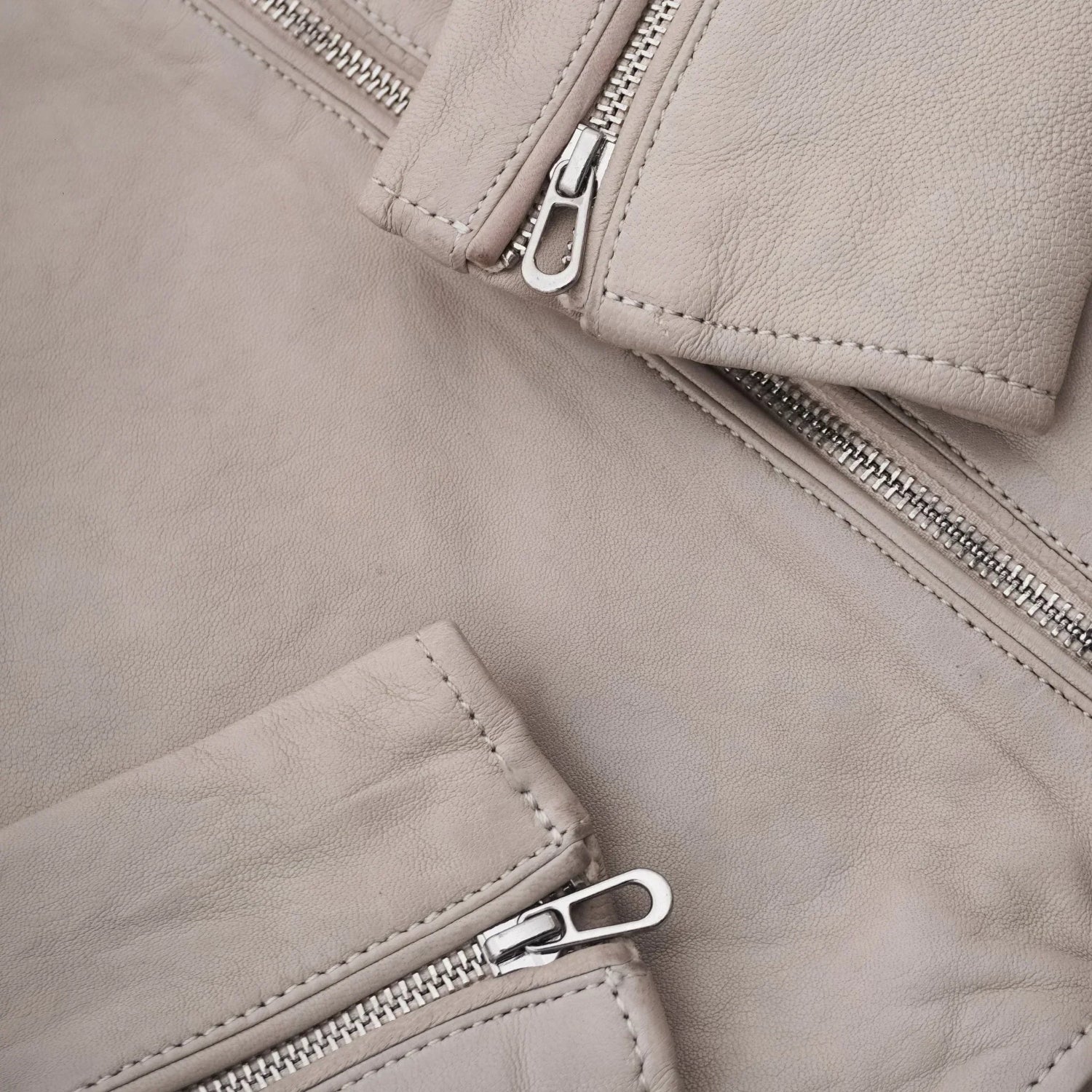 Close-up of beige women's leather jacket with silver zippers and fine stitching details.