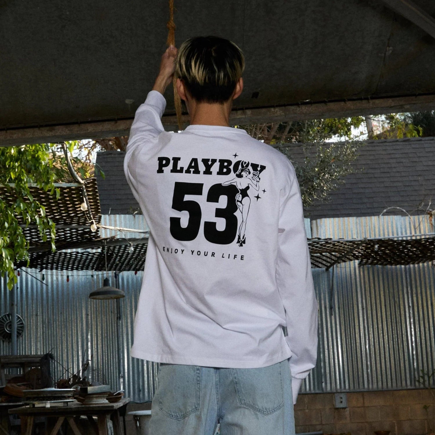 Man wearing white long sleeve graphic tee with bold 53 print and vintage pin-up illustration on back