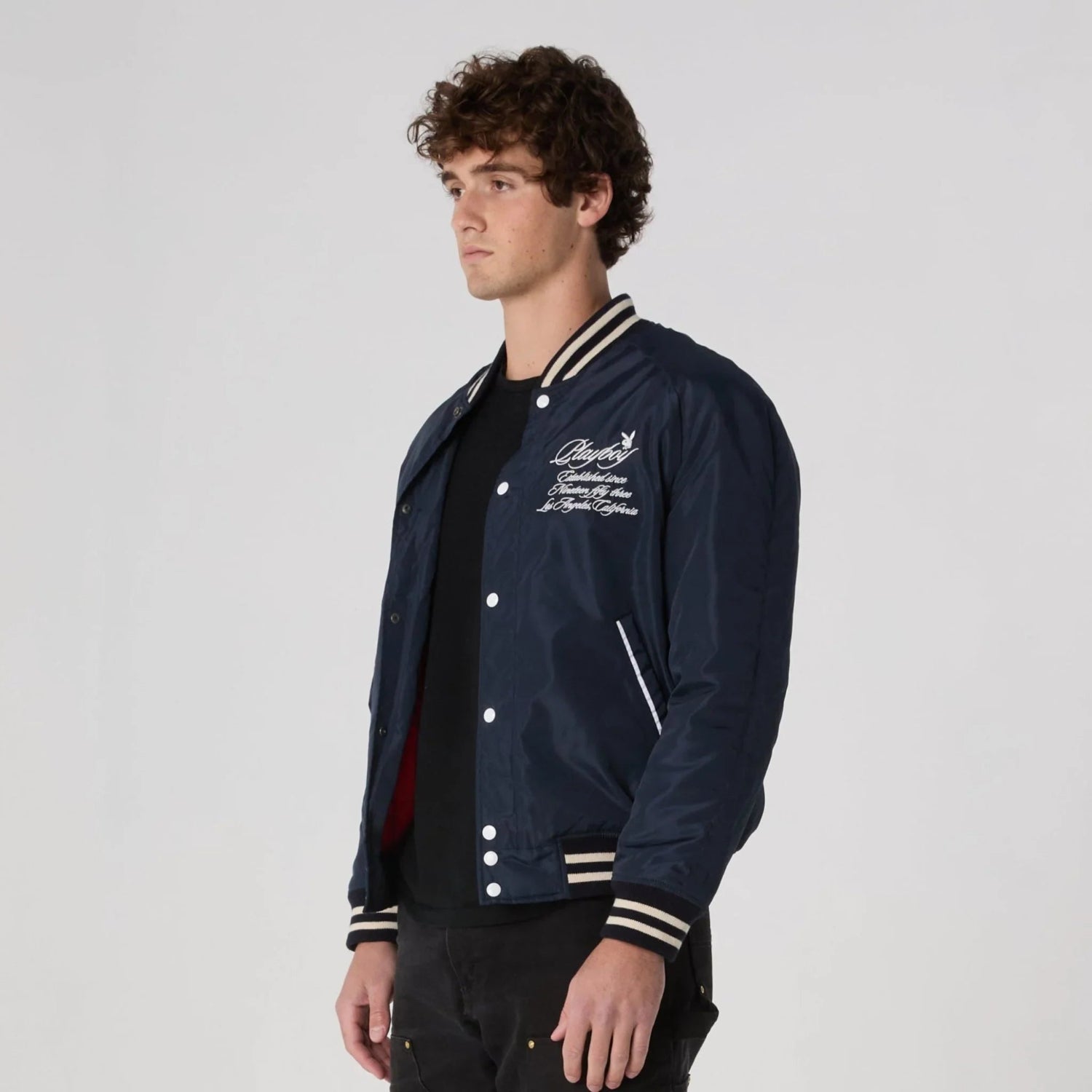 Man wearing navy blue varsity jacket with white embroidery and striped ribbed cuffs