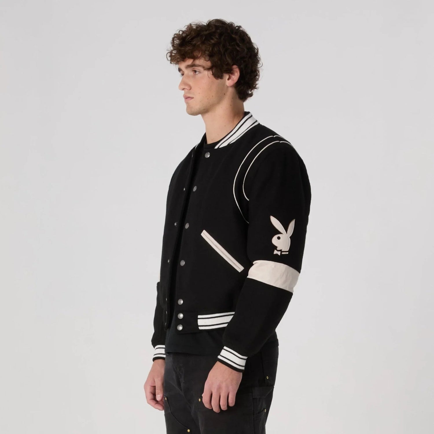 Man wearing black varsity jacket with white accents and bunny logo on sleeve
