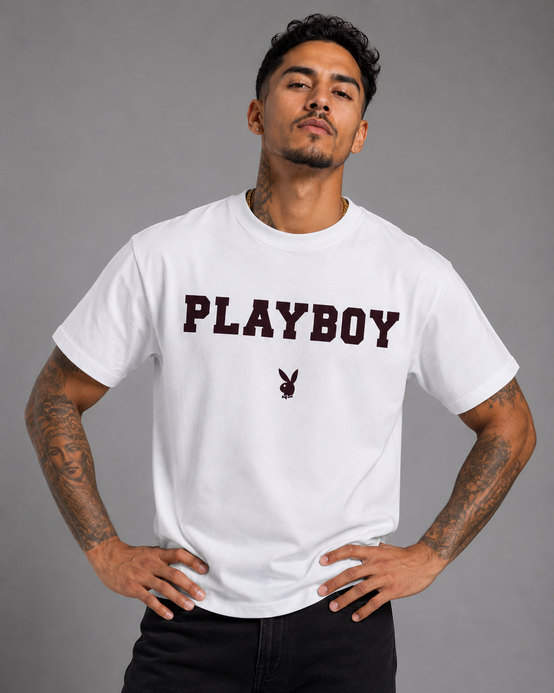 A man wearing a white short-sleeve t-shirt with 'PLAYBOY' printed across the chest in dark maroon and the classic bunny logo underneath, posed against a solid gray background.