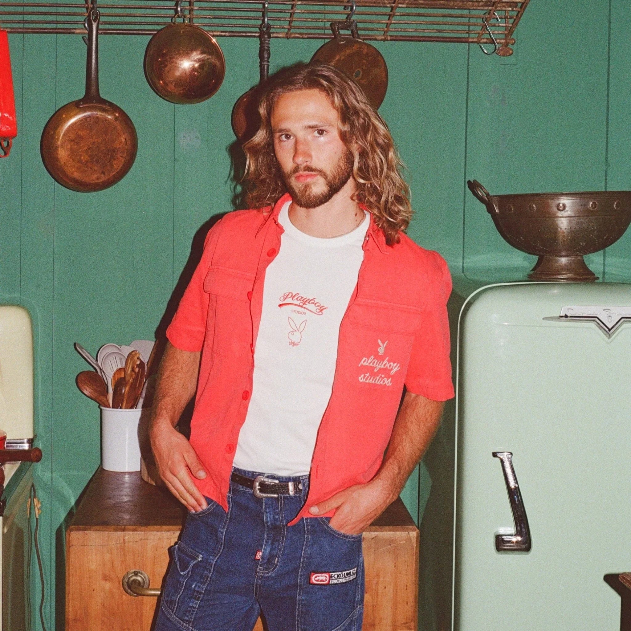 Man wearing a red button-up shirt and graphic tee in a retro kitchen setting