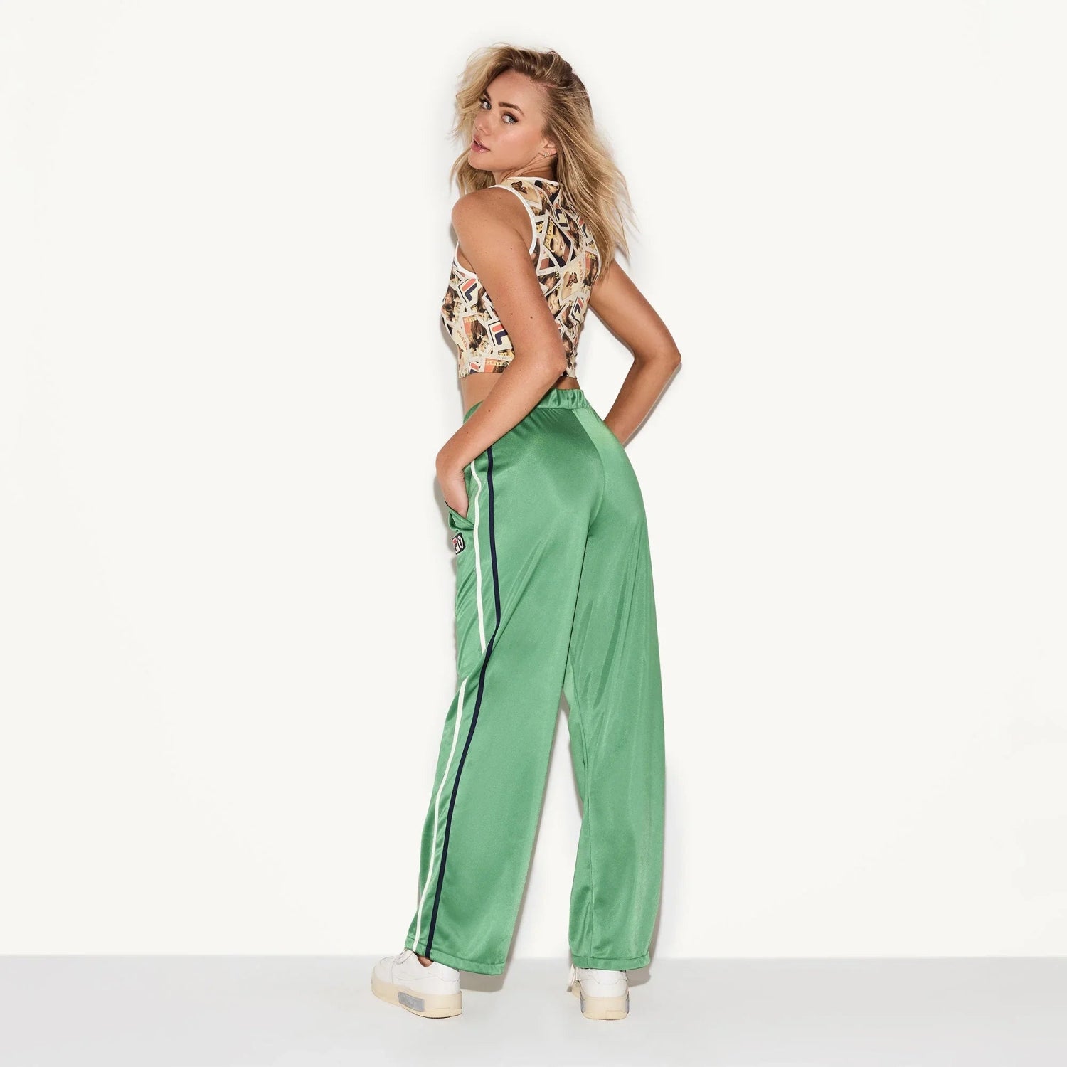 Woman wearing green satin track pants with side stripes and patch detail, casual style
