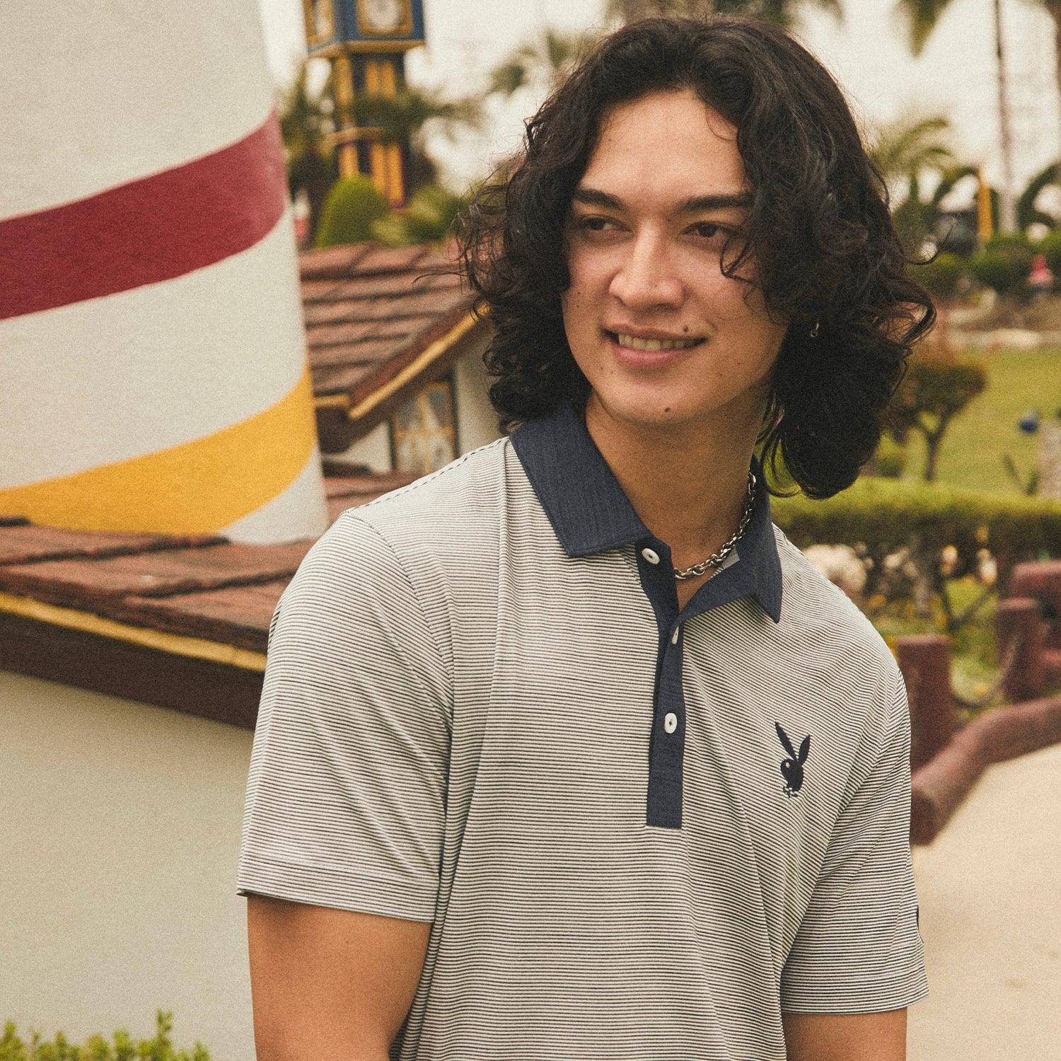Man wearing a light striped polo shirt with black collar and bunny logo outdoors