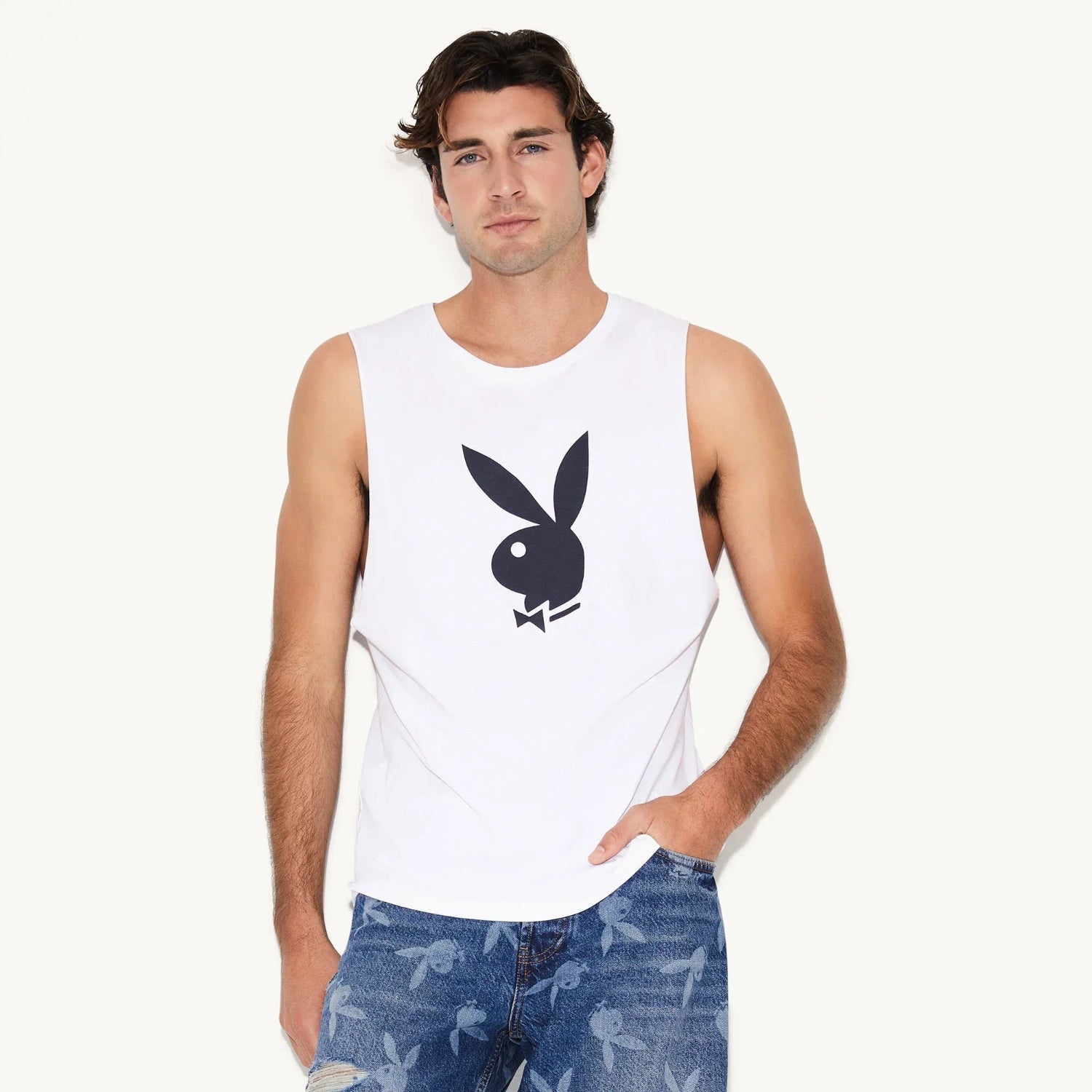 Man wearing white sleeveless tank with black rabbit head graphic and blue printed jeans