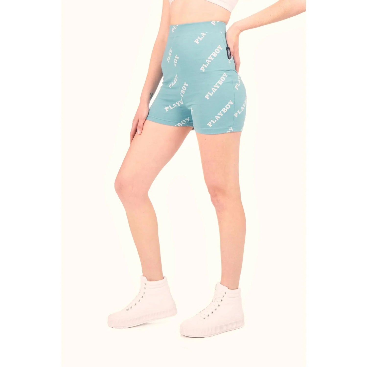 Woman wearing teal high-waisted bike shorts with white logo print and white sneakers