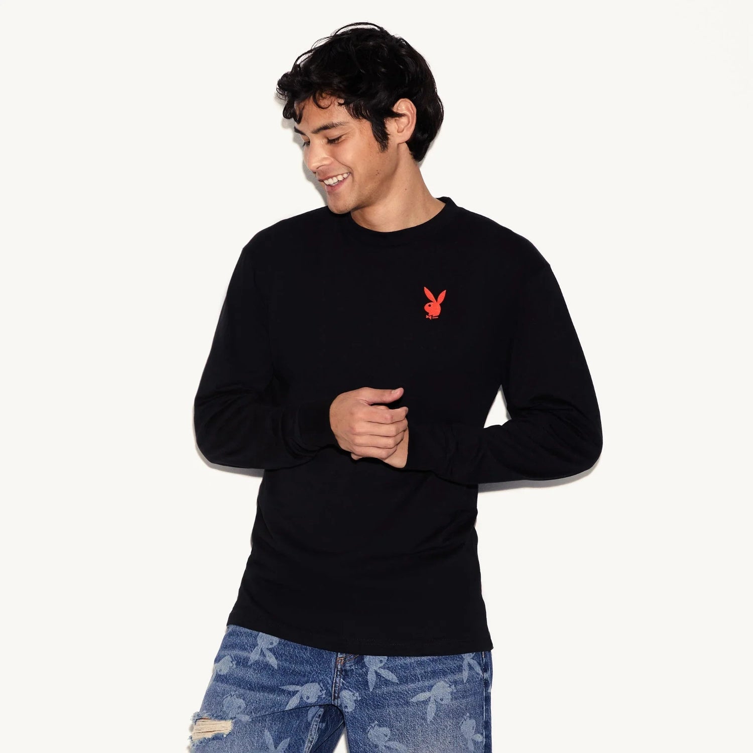 Man wearing black long sleeve t-shirt with red bunny logo and distressed blue jeans.