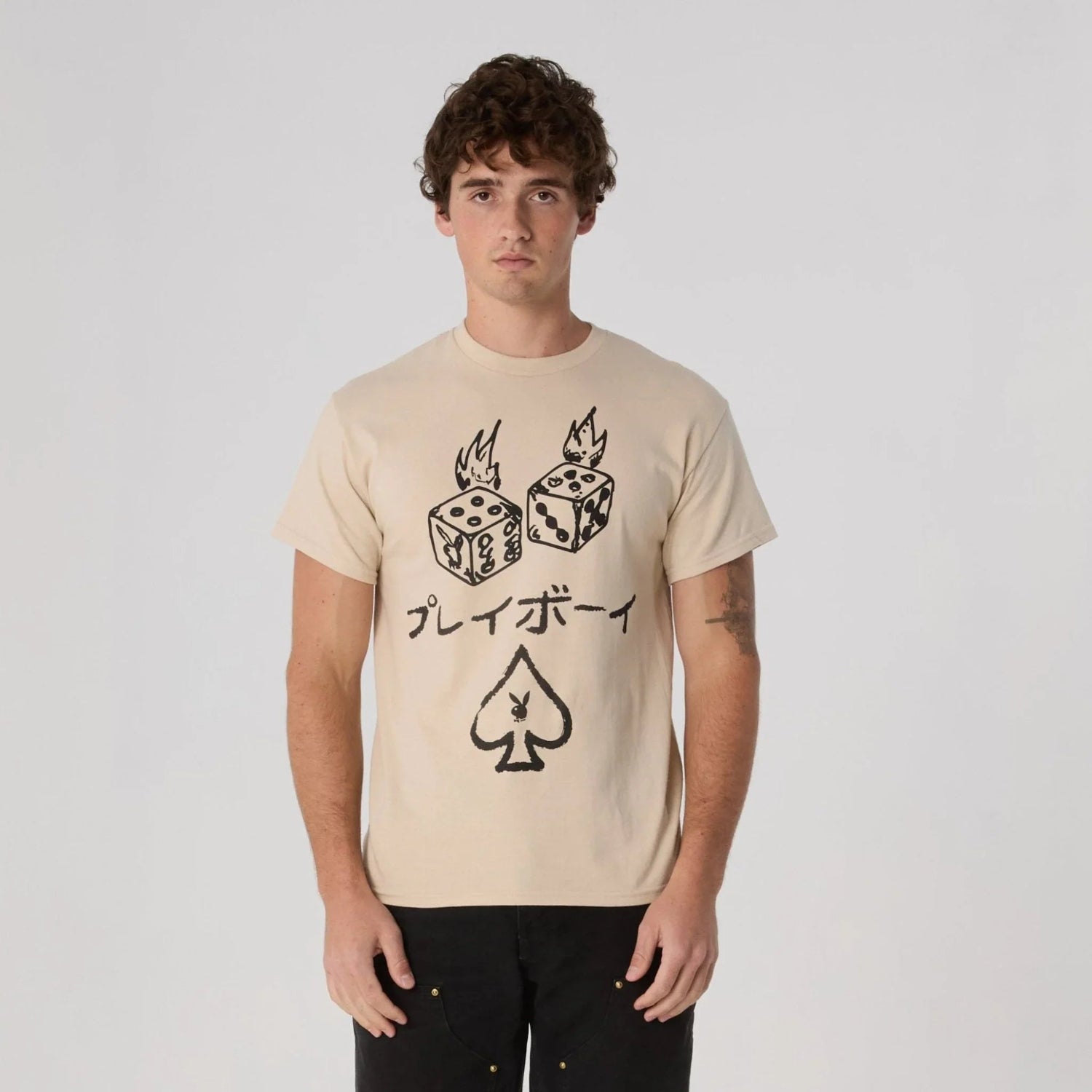 Man wearing beige graphic tee with flaming dice, Japanese text, and spade symbol