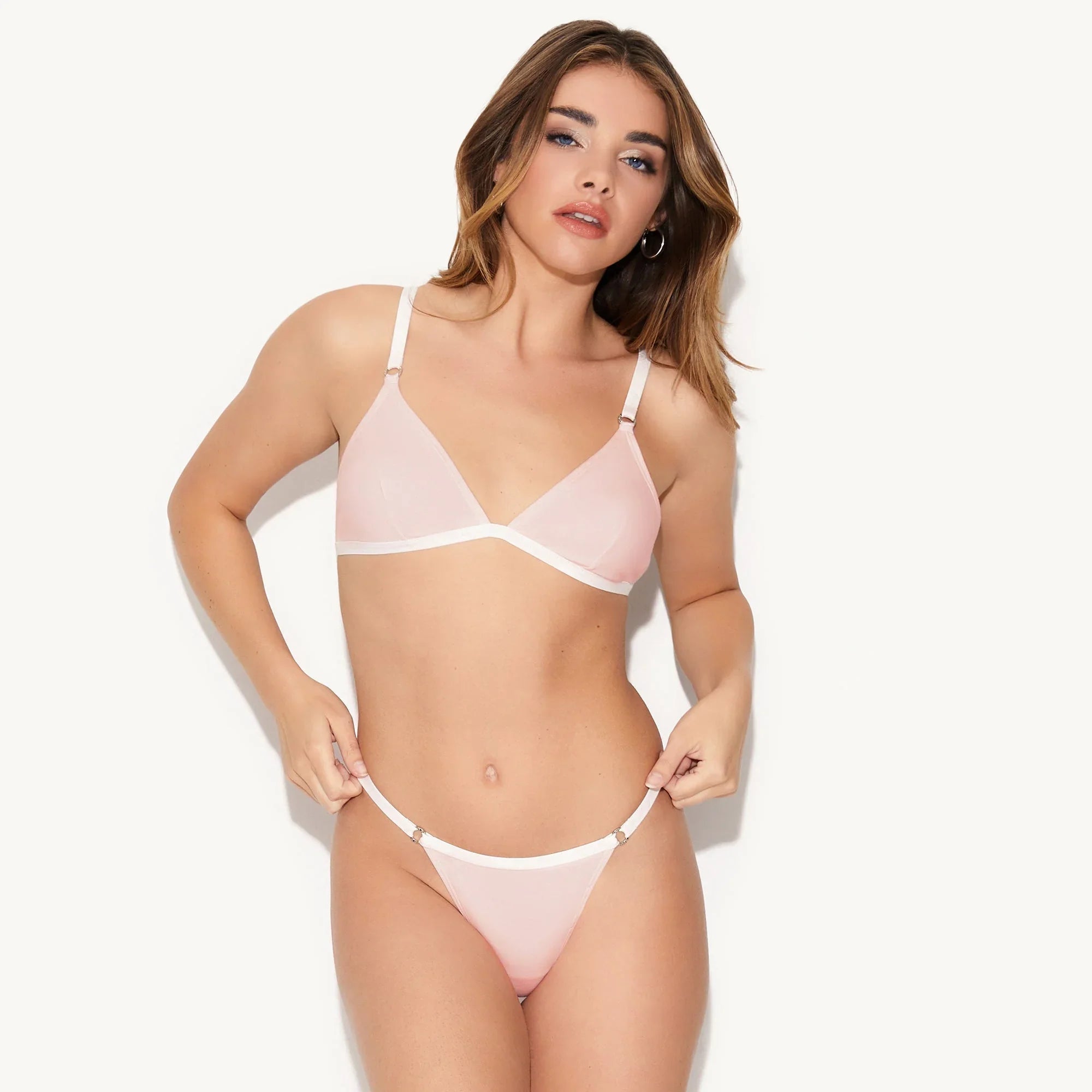 Woman modeling light pink thong underwear and matching bralette on white background