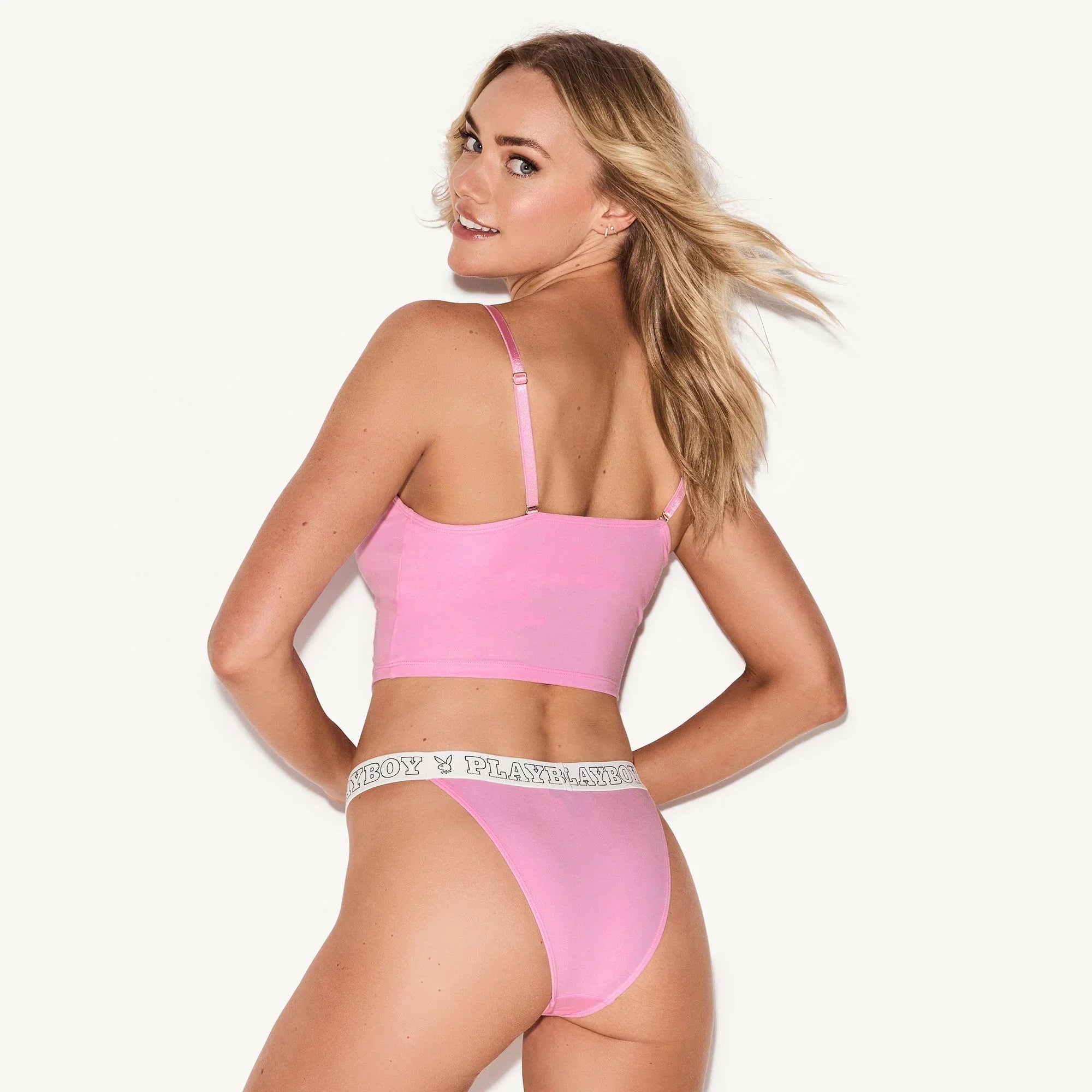Woman modeling pink cheeky bikini underwear and crop top with logo waistband on white background