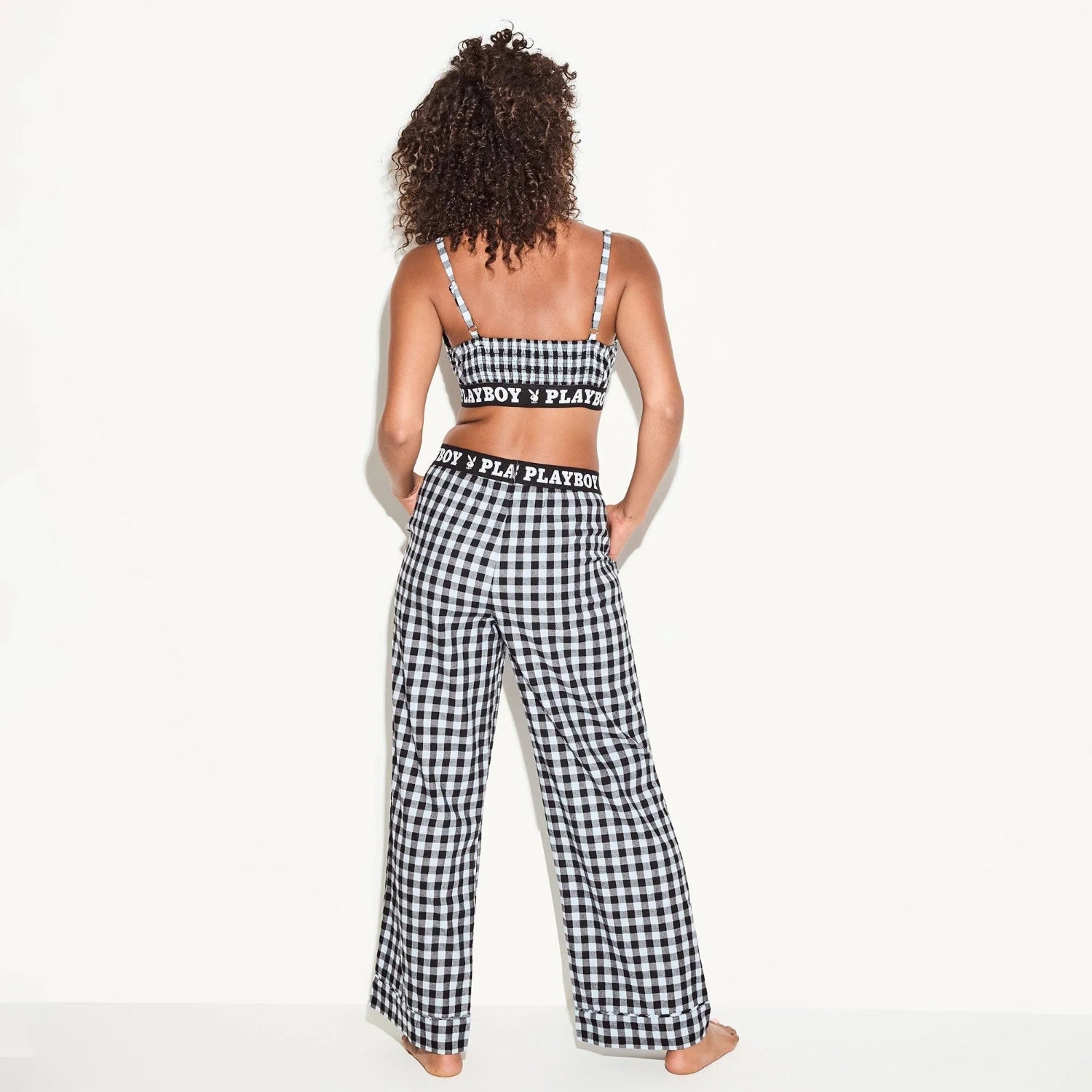 Woman modeling black and white plaid bralette and wide-leg pajama pants with logo waistband