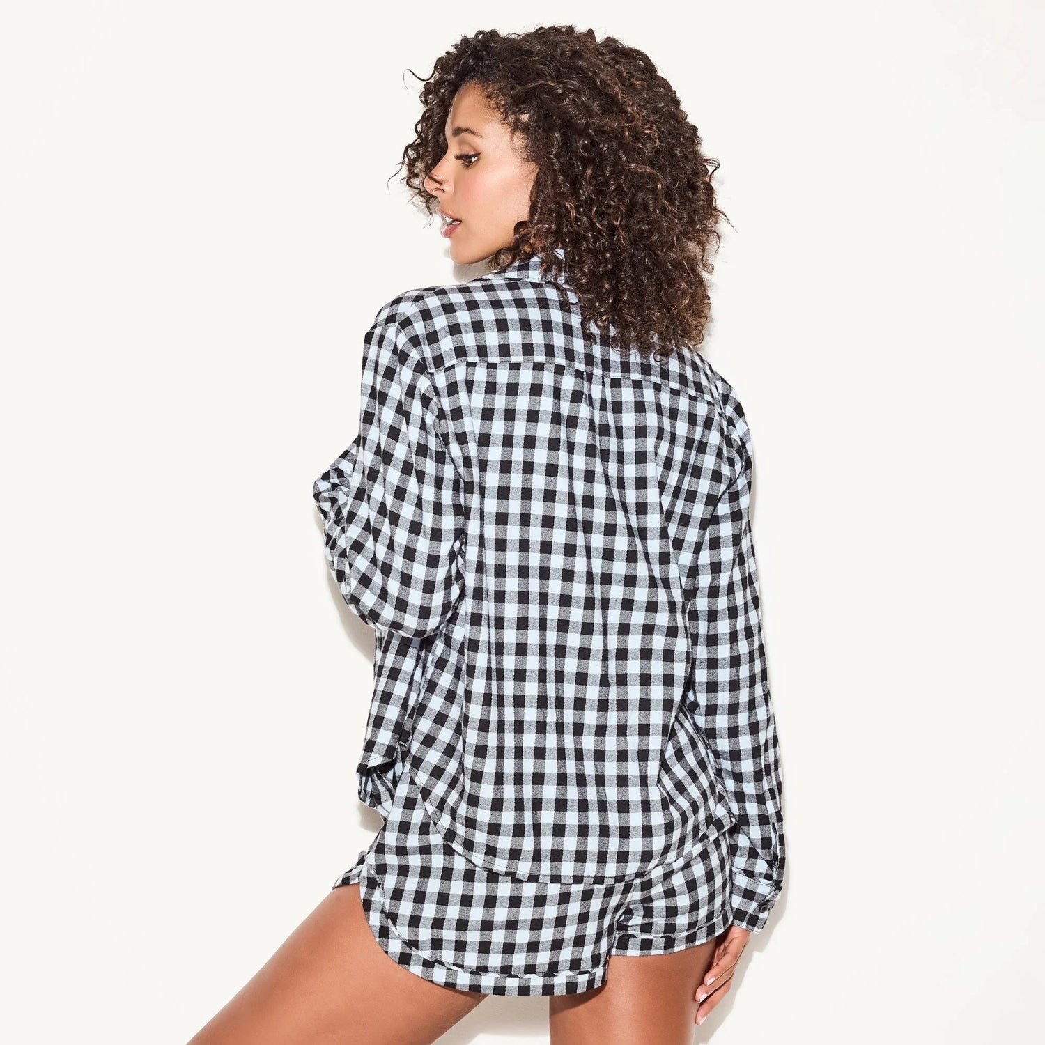Woman wearing black and white flannel sleep shirt and shorts, gingham pattern, back view