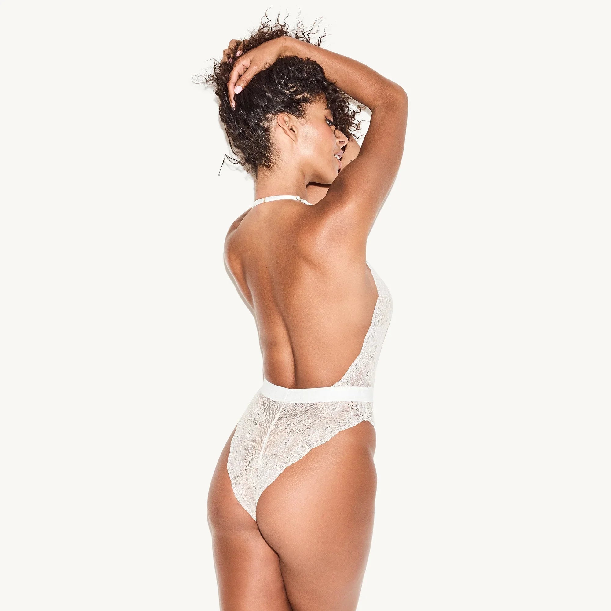 Woman modeling a white lace plunge backless bodysuit, lingerie against white background