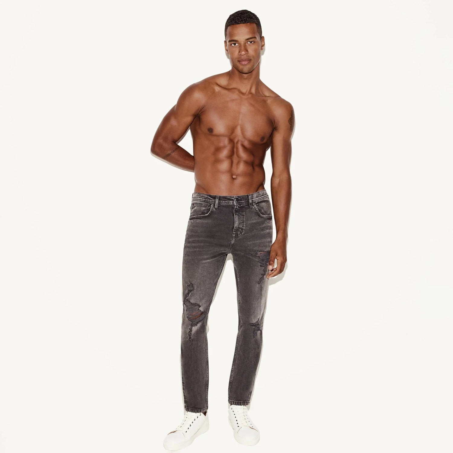 Man modeling grey skinny distressed jeans with knee rip, white sneakers, plain background