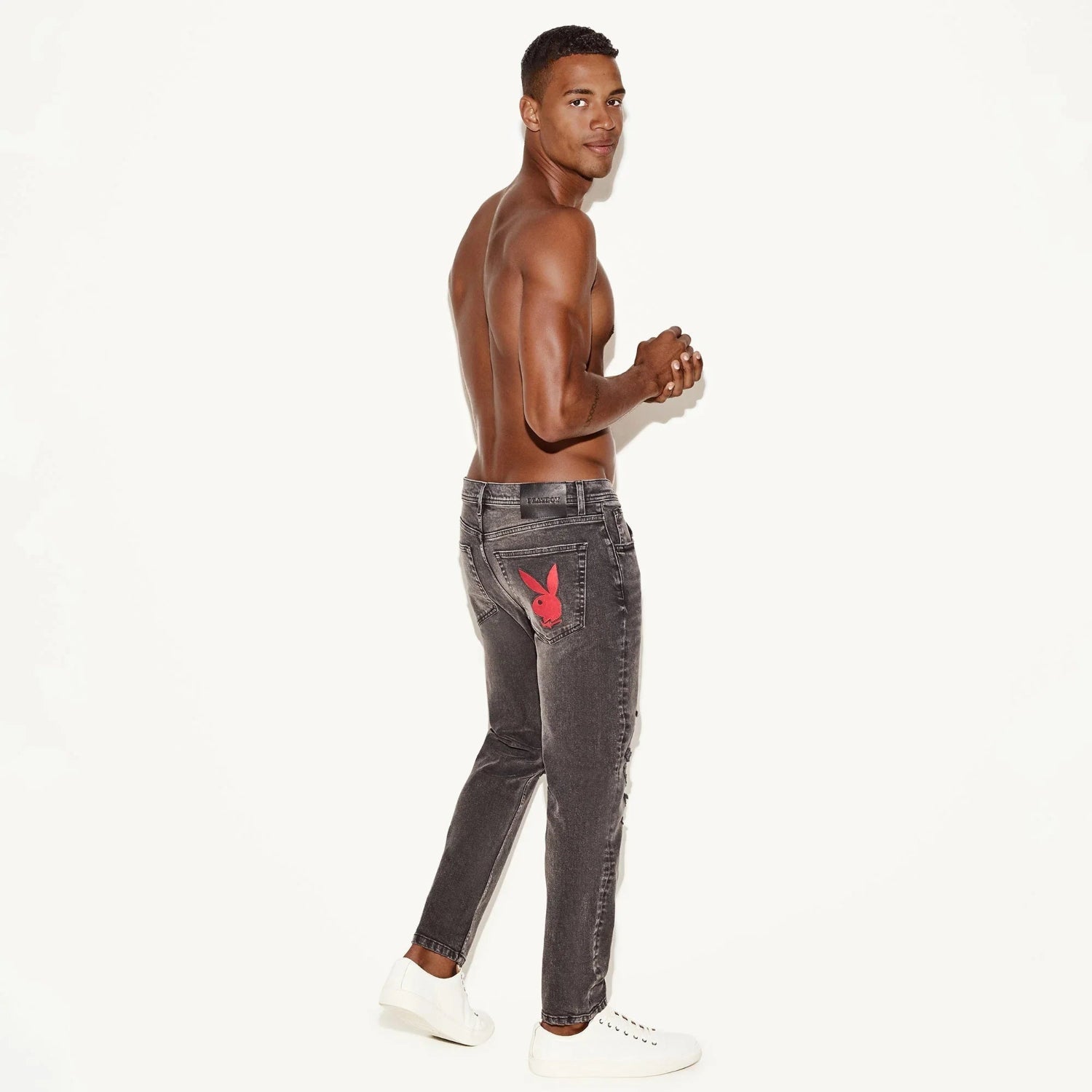 Man modeling distressed grey skinny jeans with red bunny logo on back pocket, white shoes