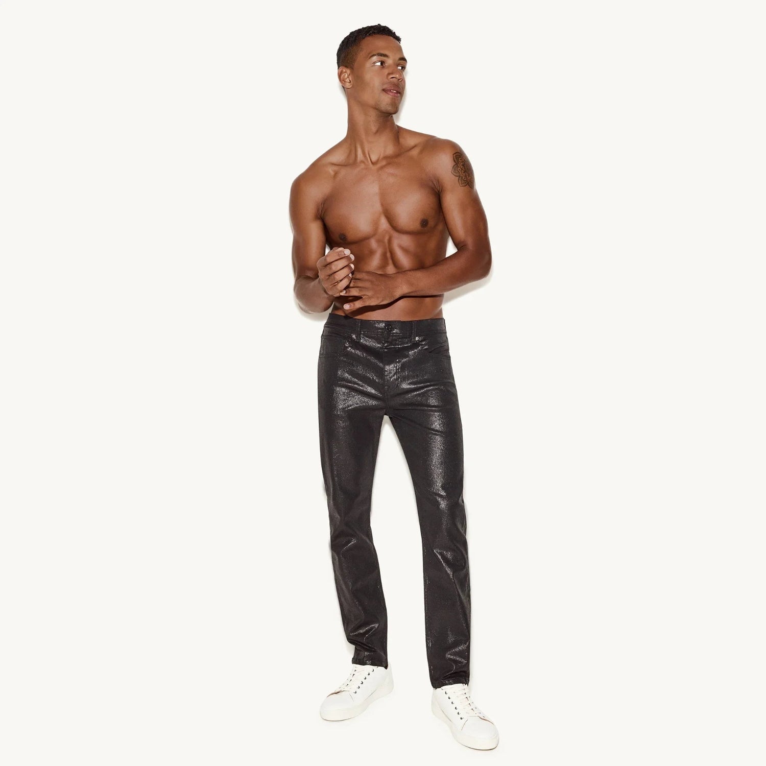 Shirtless man modeling black waxed skinny jeans and white sneakers on white background