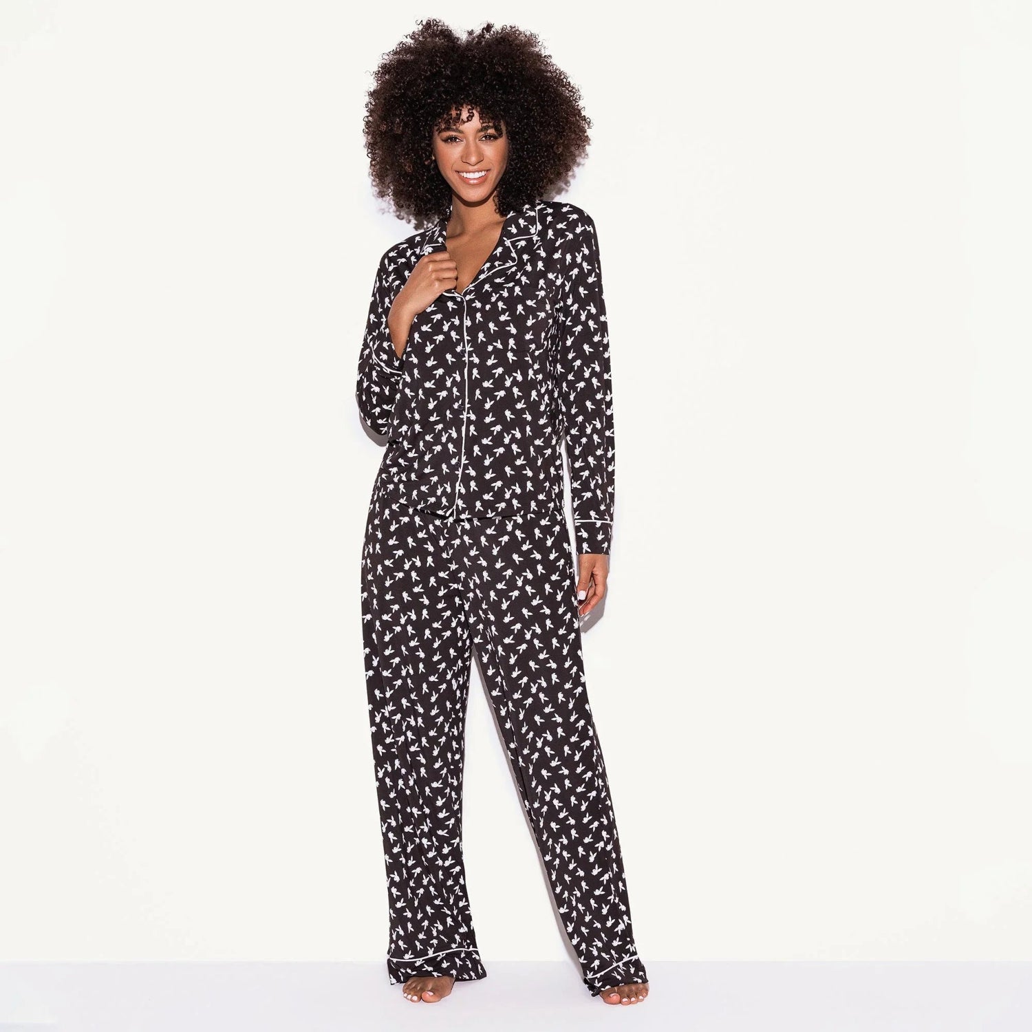 Woman wearing black pajama set with white bunny print and white piping, standing against white background