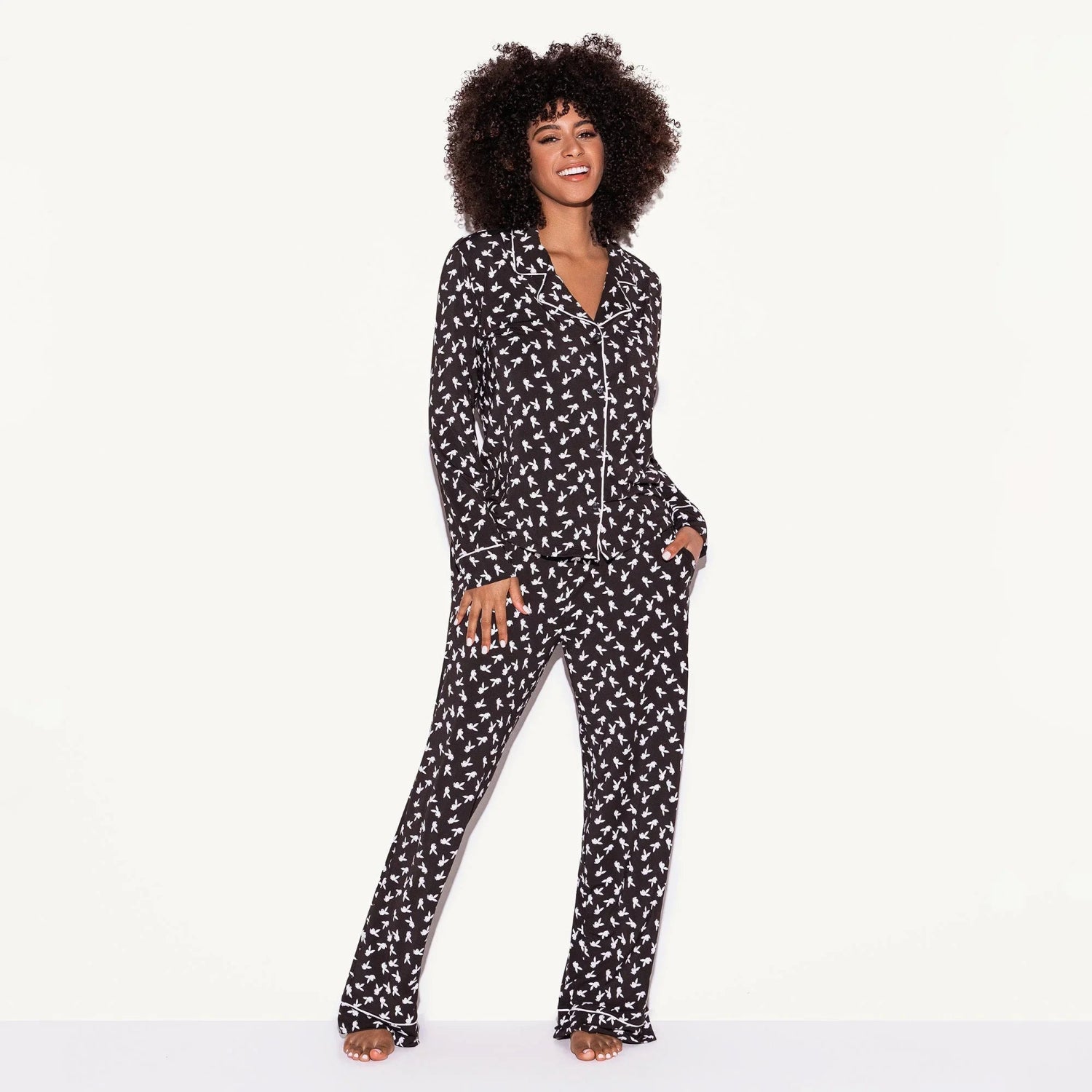 Woman wearing black pajama set with white bunny print, long sleeves and pants, studio background