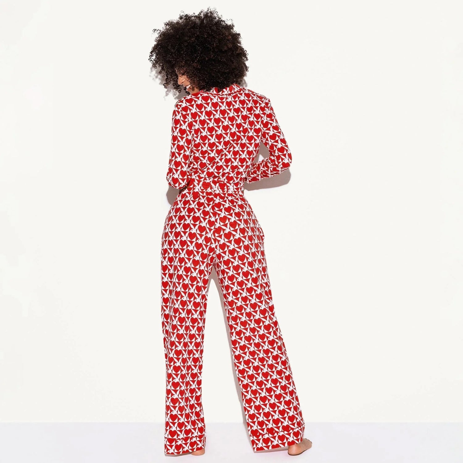 Woman wearing red long-sleeve pajama set with white graphic print, standing barefoot