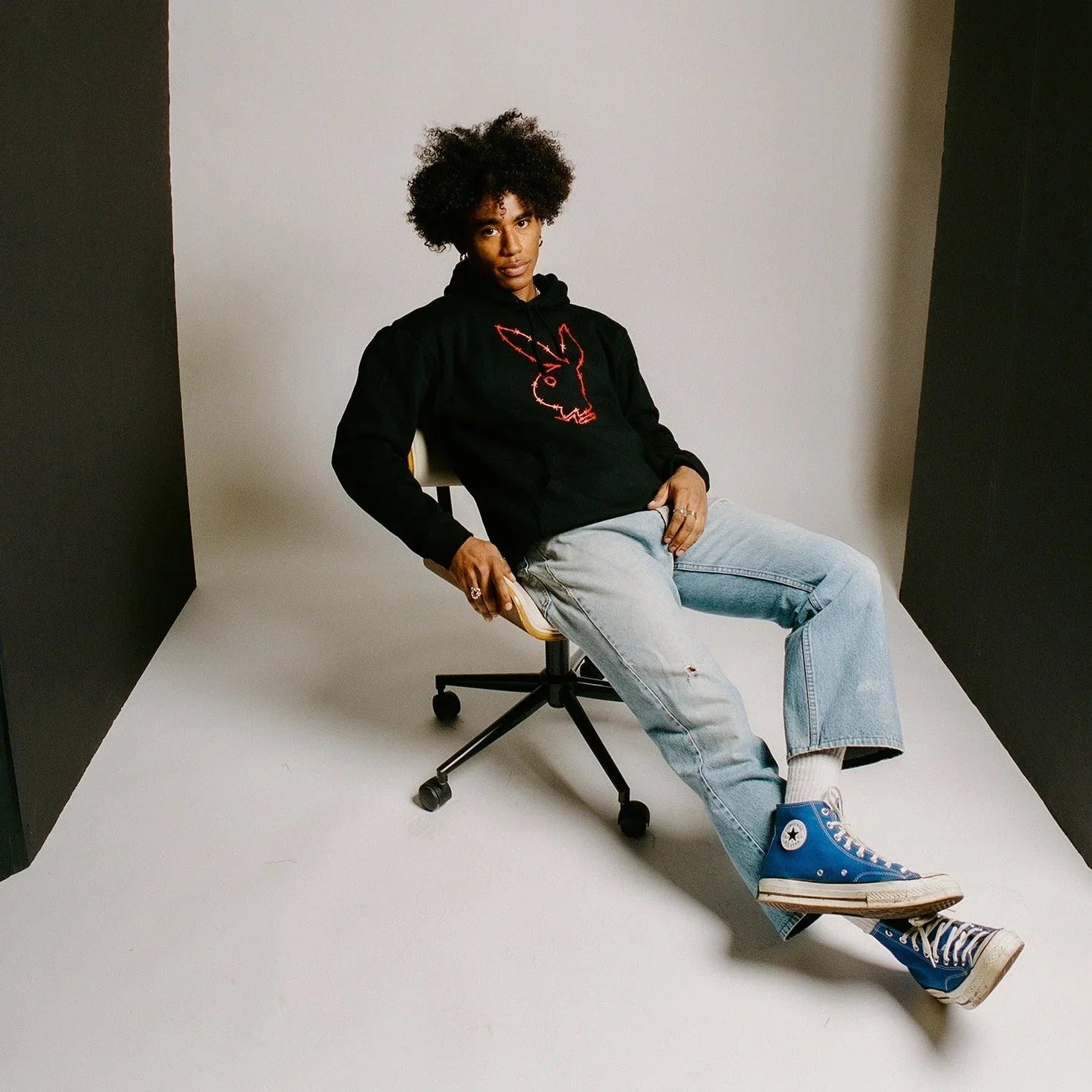Man wearing black hoodie with red rabbit head outline, light blue jeans, and blue sneakers