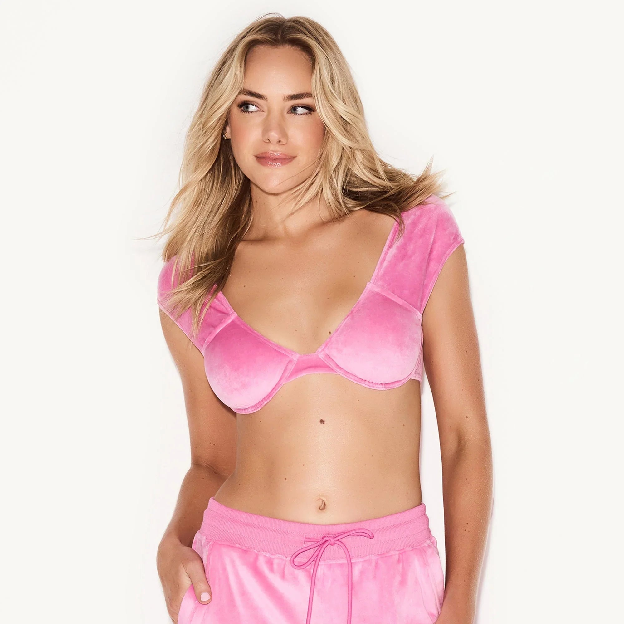 Woman wearing a pink velour underwire cap sleeve bra and matching lounge pants
