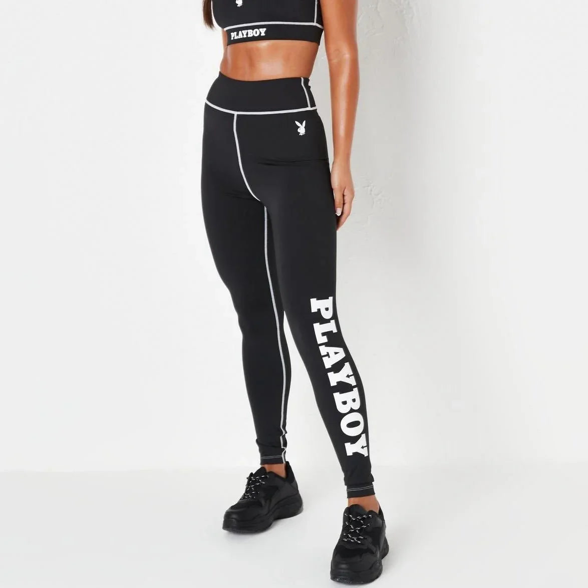 Woman wearing black high-waisted leggings with white PLAYBOY text and outline seams