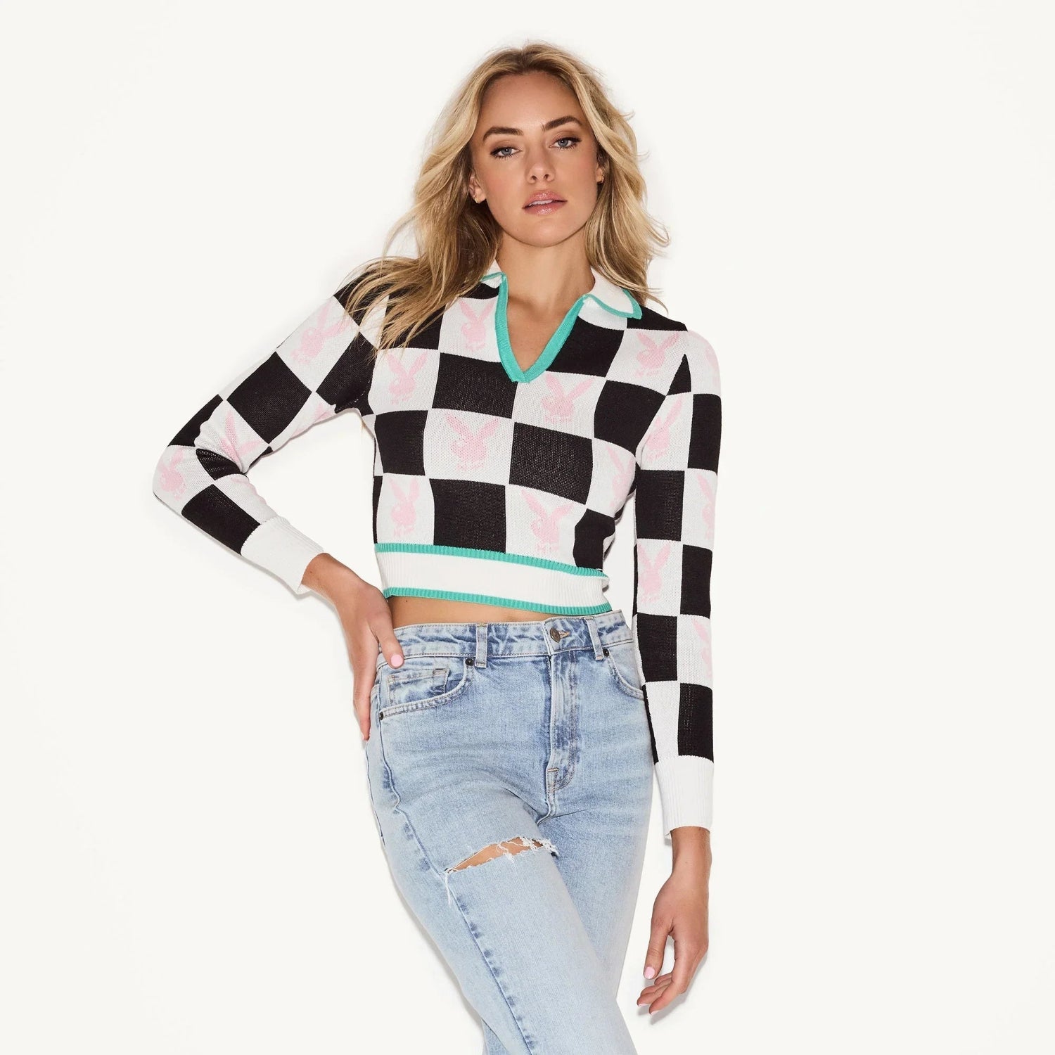 Woman wearing a black and white checkerboard crop top with pink bunny logos and ripped jeans