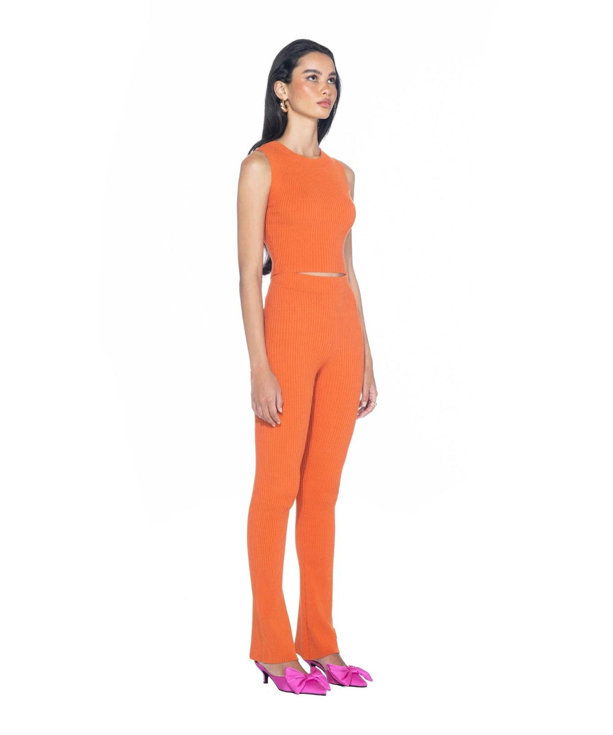 Woman wearing orange ribbed cropped tank top and pants with pink bow heels on white background