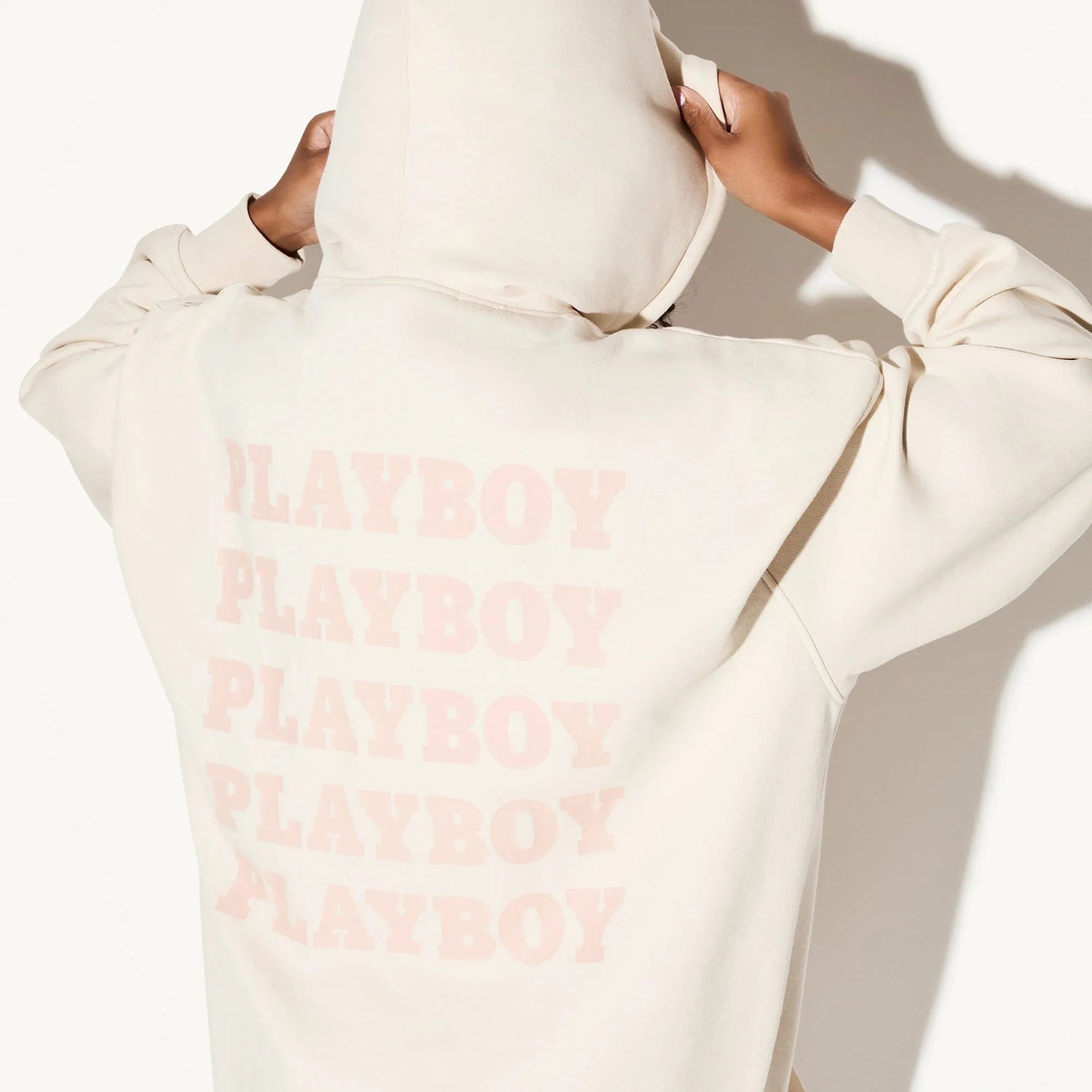 Back view of woman wearing cream hoodie dress with repeat block print text design