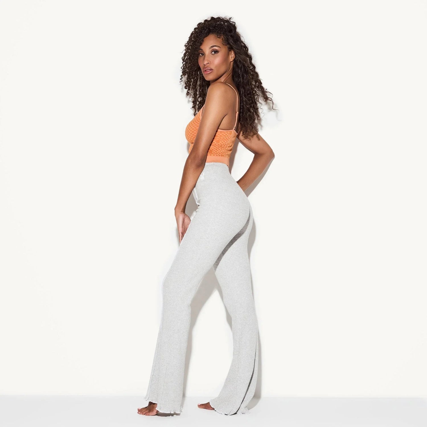 Woman modeling light gray ribbed flare pants with high waist, standing against white background.