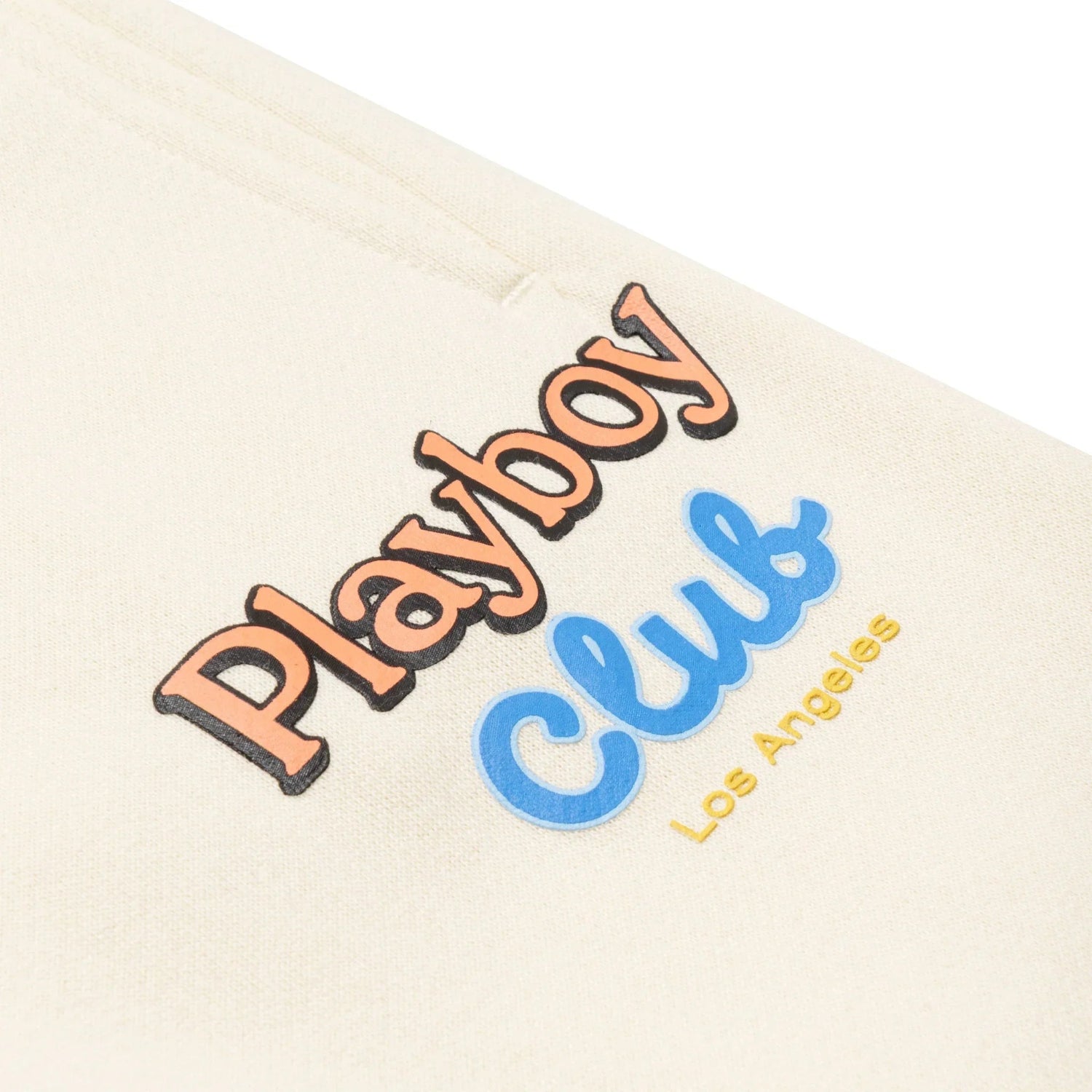 Close-up of beige sweatpants with 'Playboy Club Los Angeles' graphic text detail.