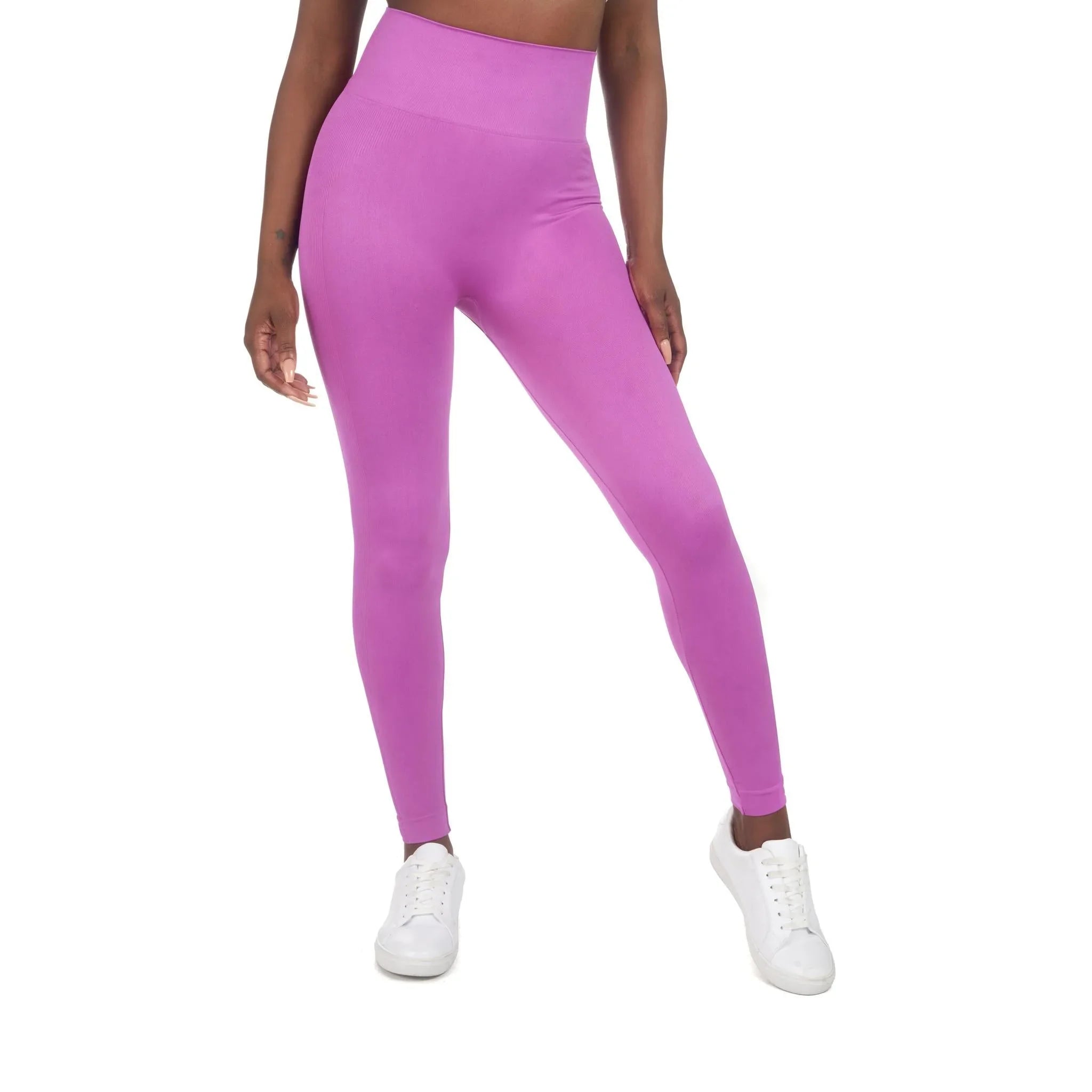Woman wearing high-waisted pink sport leggings and white sneakers on white background
