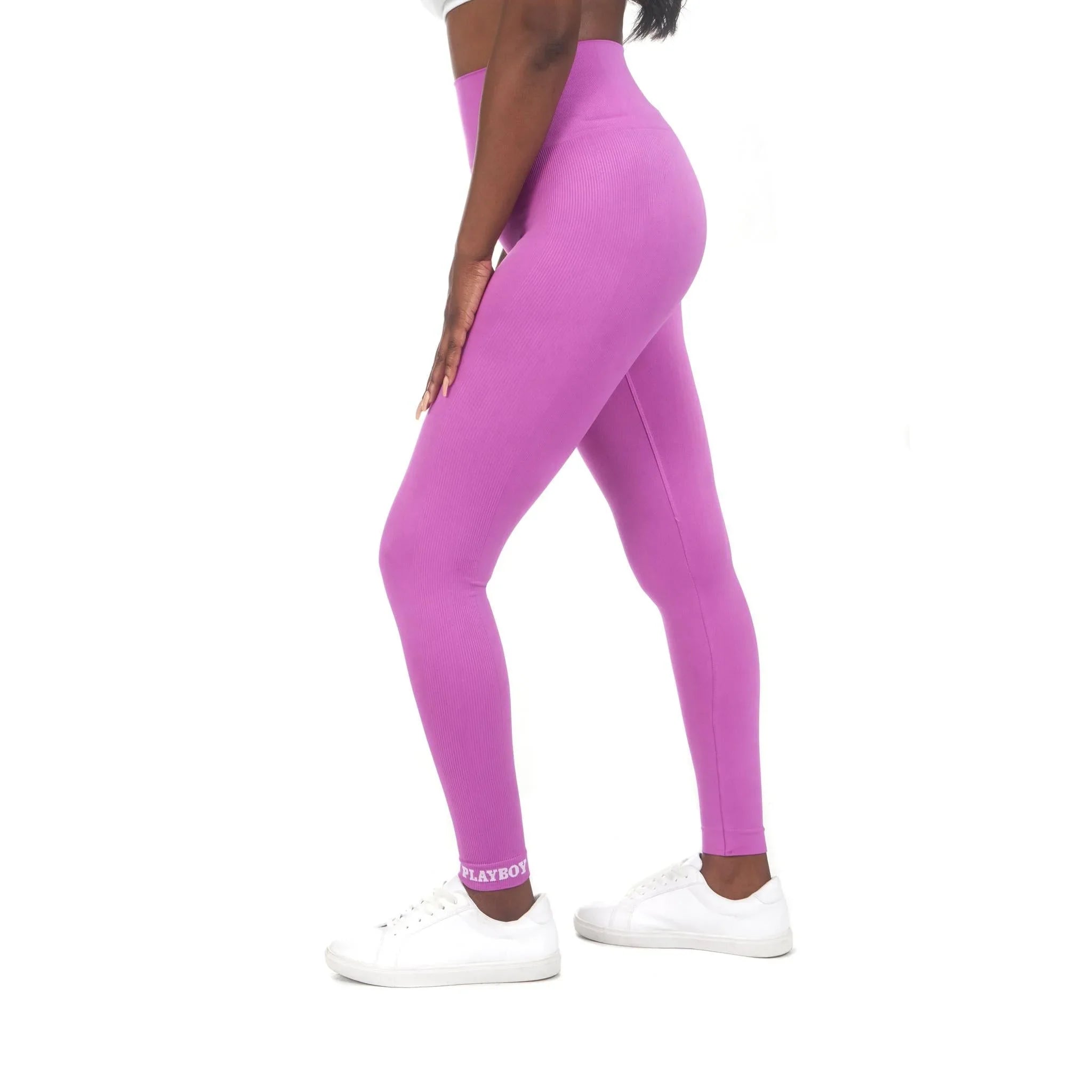 Woman wearing high-waisted purple sport leggings with logo and white sneakers, side view