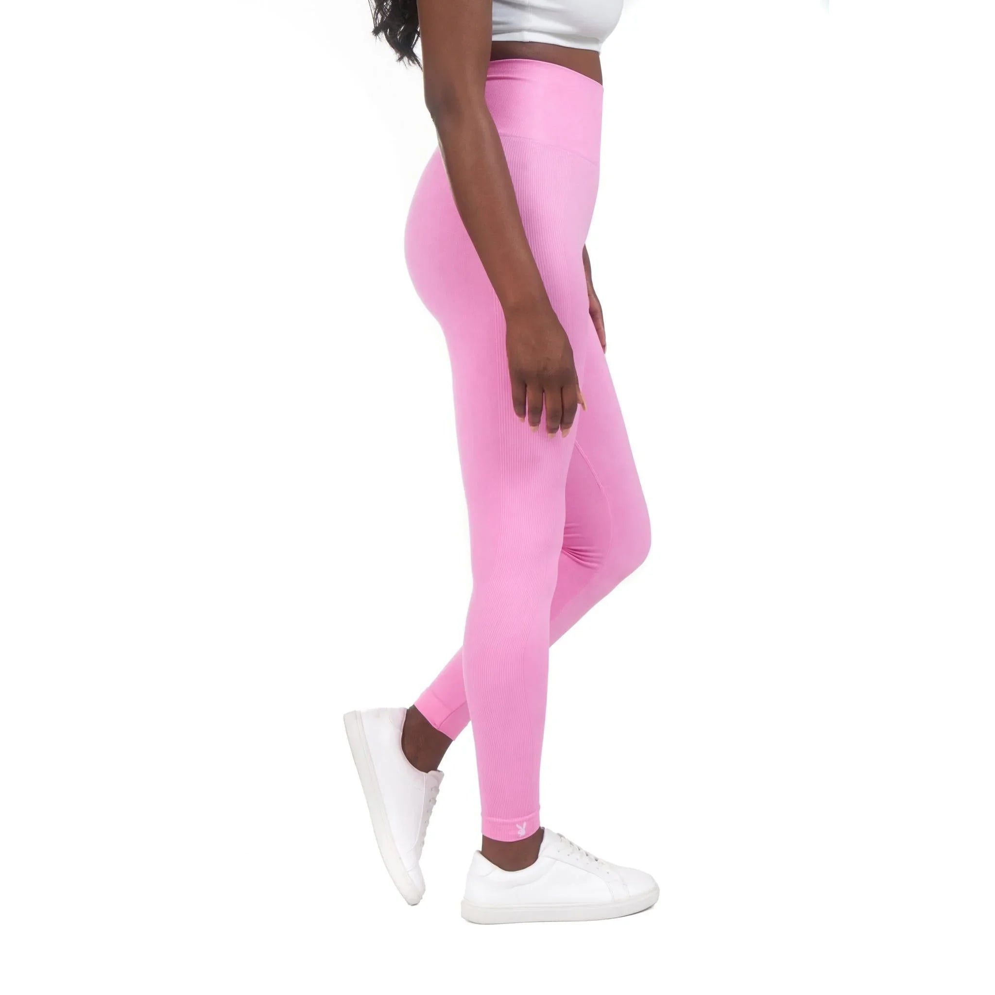 Woman wearing high-waisted pink sports leggings and white sneakers on white background