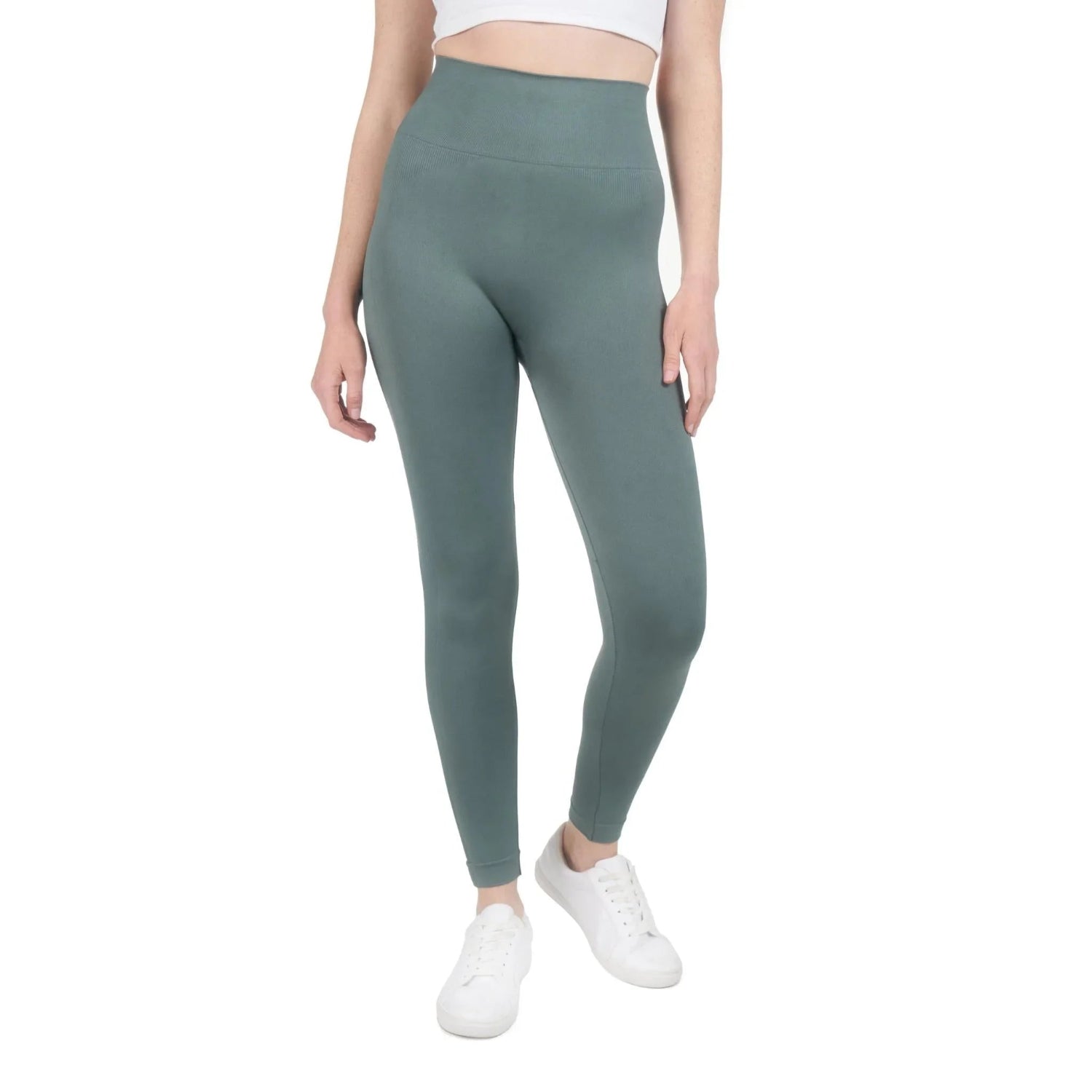 Woman wearing high-waisted green sports leggings and white sneakers on white background