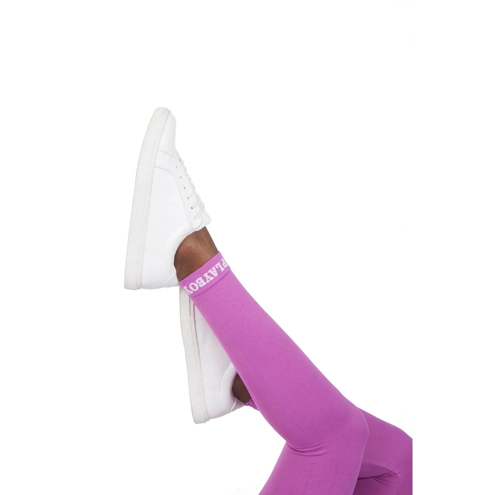 Woman wearing pink ribbed sport leggings with white sneakers, legs crossed against white background