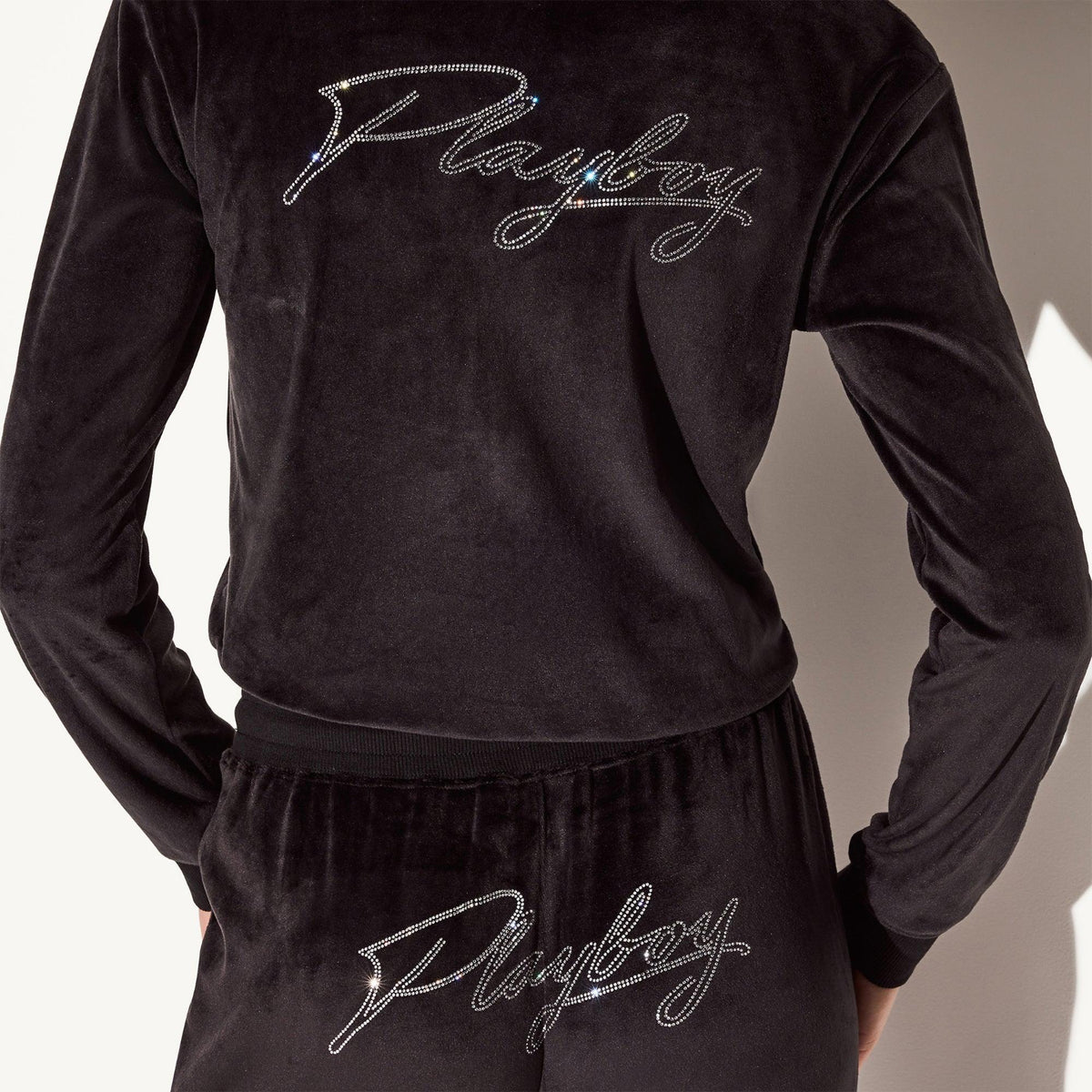 Back view of woman wearing black velour jacket and pants with rhinestone script logo