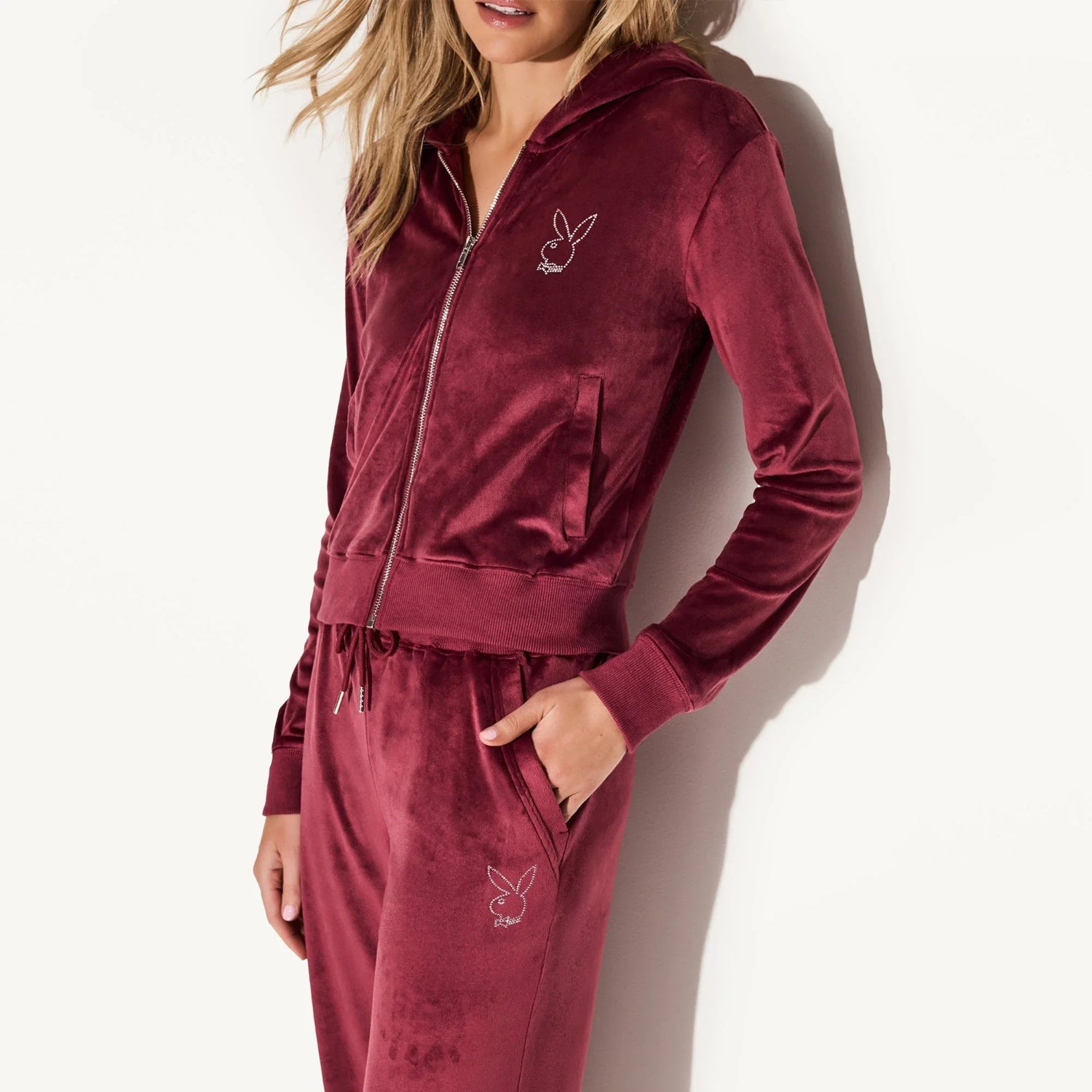 Woman wearing maroon velour zip-up jacket and matching joggers with bunny logo