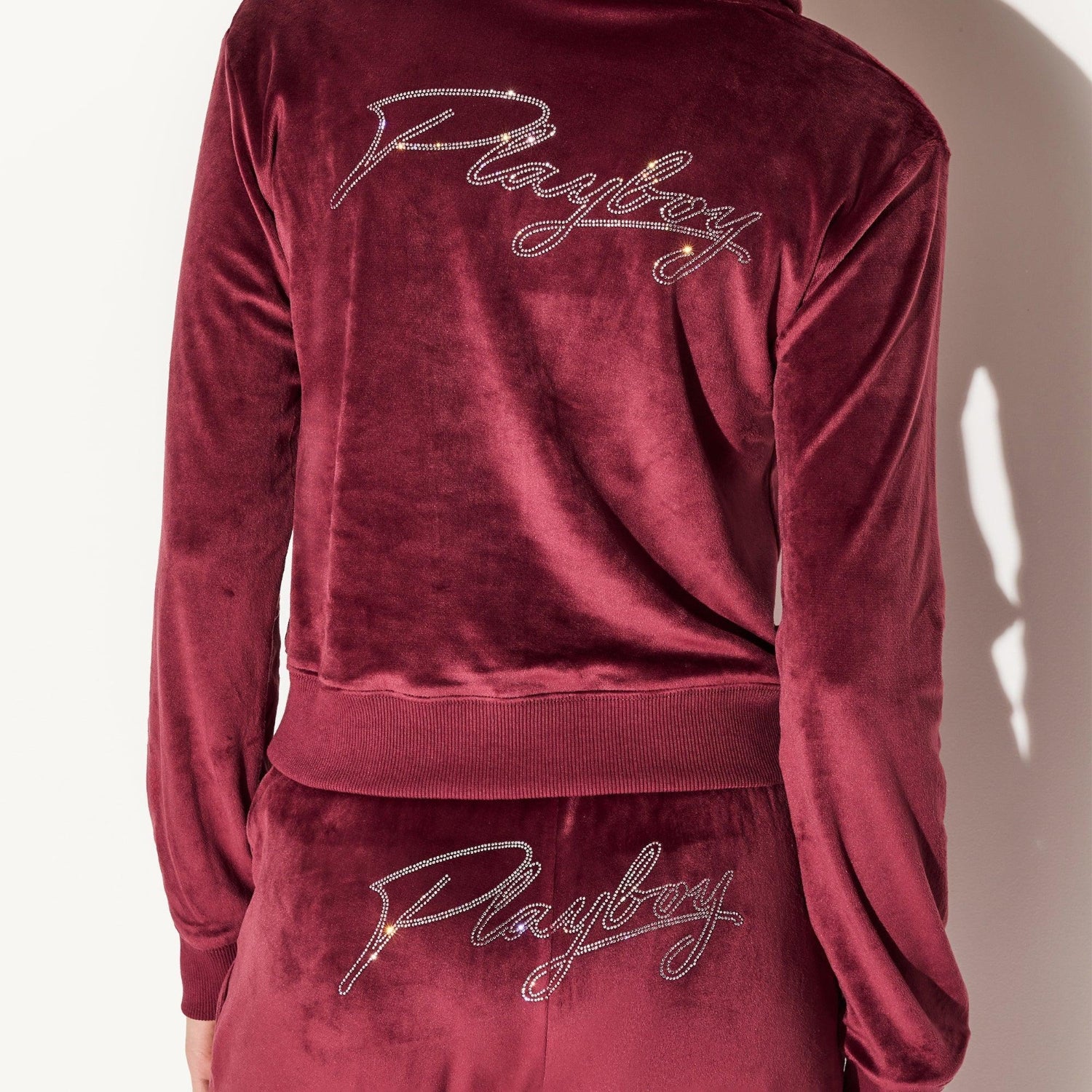 Back view of a women's burgundy velour jacket and pants set with rhinestone script text.